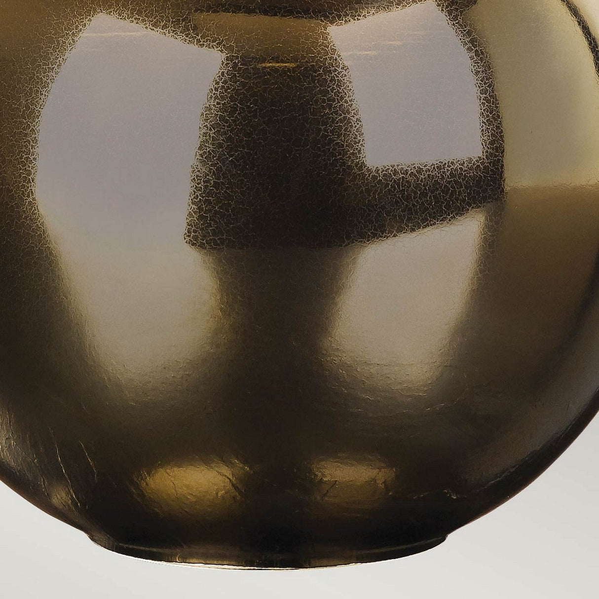 Close-up of the glossy, rounded metal surface of the Ottoman 1 Light Table Lamp, featuring a textured pattern that evokes a bronze finish. The surface gleams as it catches the light, reminiscent of an elegant table lamp base, with a slightly tarnished look that creates an intriguing blend of light and dark tones.