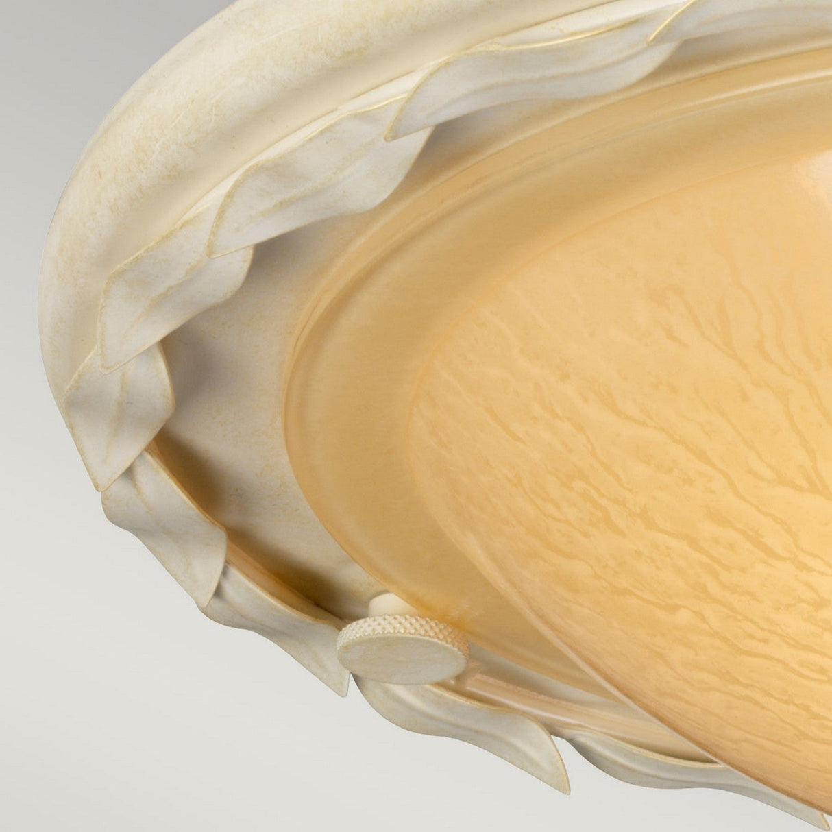 Close-up of the Olivia 1 Light Flush in an ivory and gold patina, showcasing a creamy, carved leafy edge and a textured, amber-colored glass shade. A small round switch is visible on the rim, emphasizing its exquisite handmade craftsmanship.