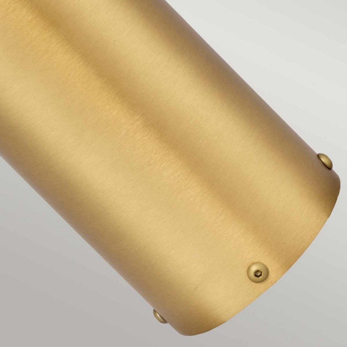 A close-up of the Paignton 1 Light Bollard in brushed brass displays its cylindrical form with a smooth texture and beveled edges, highlighting its robust solid brass construction. Small, round-headed screws are visible on one side, set against a neutral gray backdrop, conveying the sophisticated craftsmanship typical of high-quality outdoor lighting fixtures.