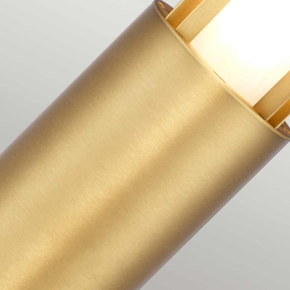 Close-up of the Paignton 1 Light Bollard in brushed brass, featuring a frosted light that emits a warm glow. The lamp has a matte finish, and the image is angled to showcase the upper portion against a neutral light gray background, bringing to mind elegant outdoor lighting.