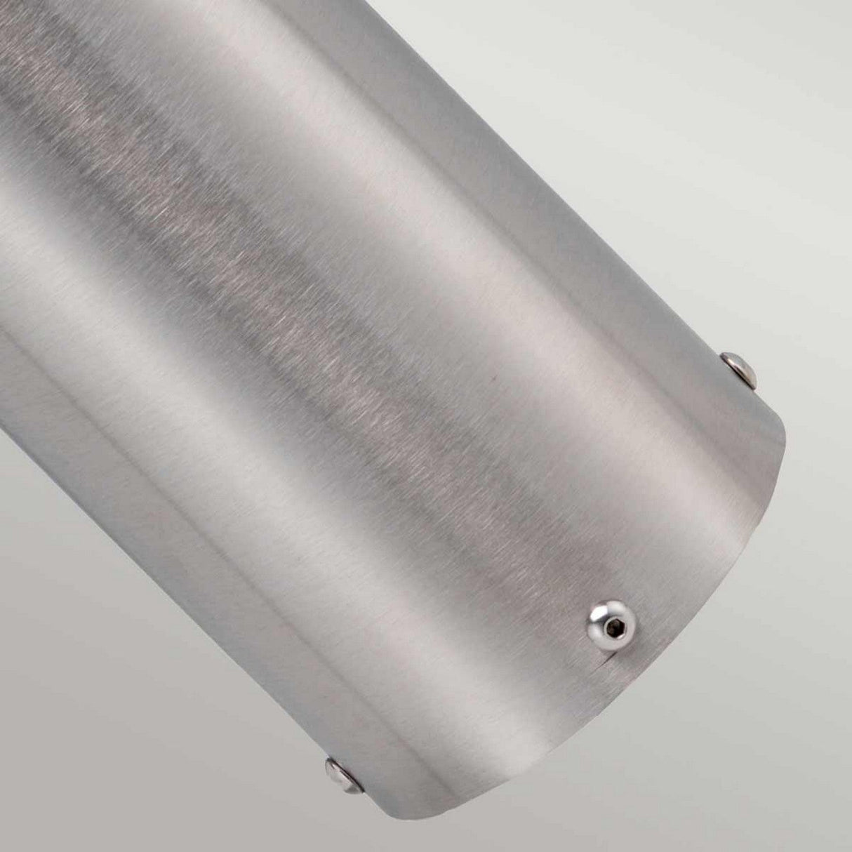 A close-up view of the Paignton 1 Light Bollard - Stainless Steel reveals its smooth, slightly reflective surface. This stainless steel cylinder is secured with small round screws and features frosted glass accents, all set against a light gray background.