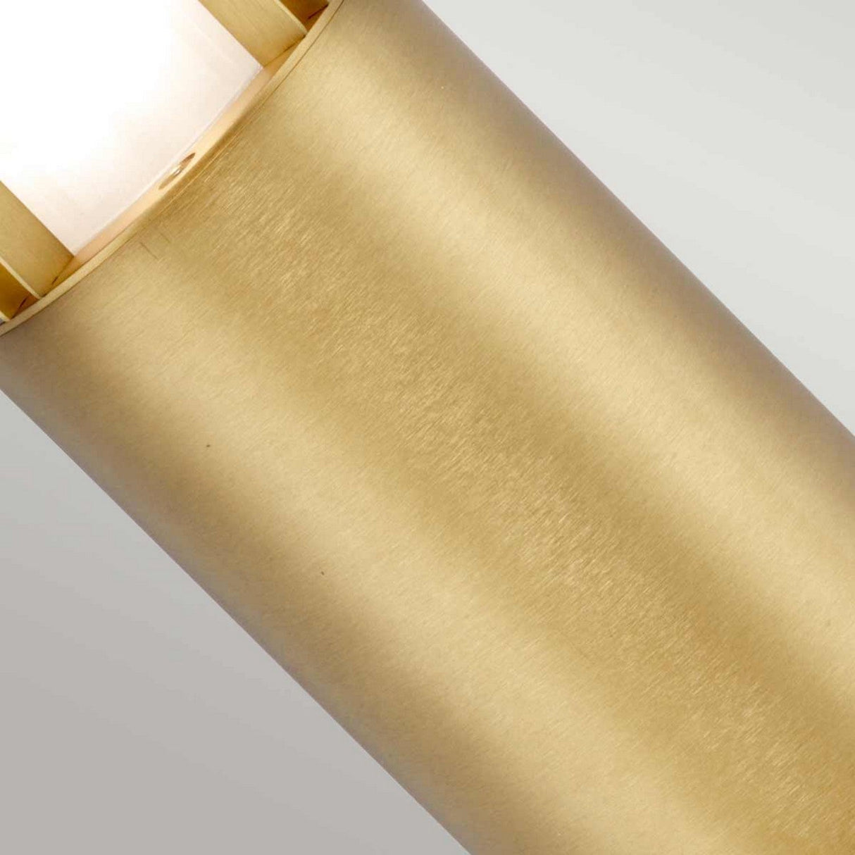 Close-up of the Paignton 1 Light Mini Bollard in brushed brass, a cylindrical metal structure with a smooth finish and a light emitting from the top edge. This piece provides an inviting warmth, ideal for outdoor lighting.