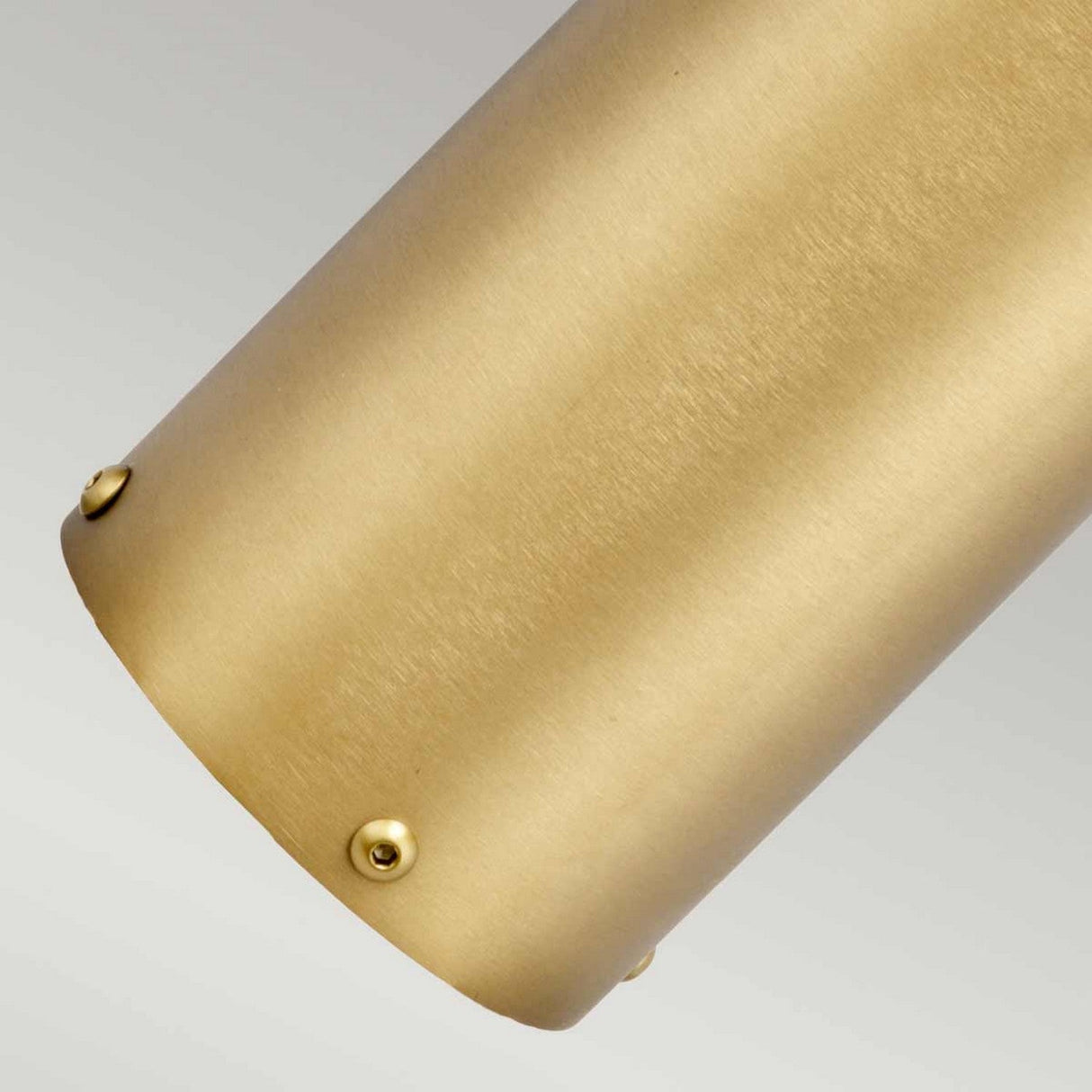 A close-up view of the Paignton 1 Light Mini Bollard in a brushed brass finish, showcasing its cylindrical shape and small rounded screws along the edge, positioned diagonally against a gray background.