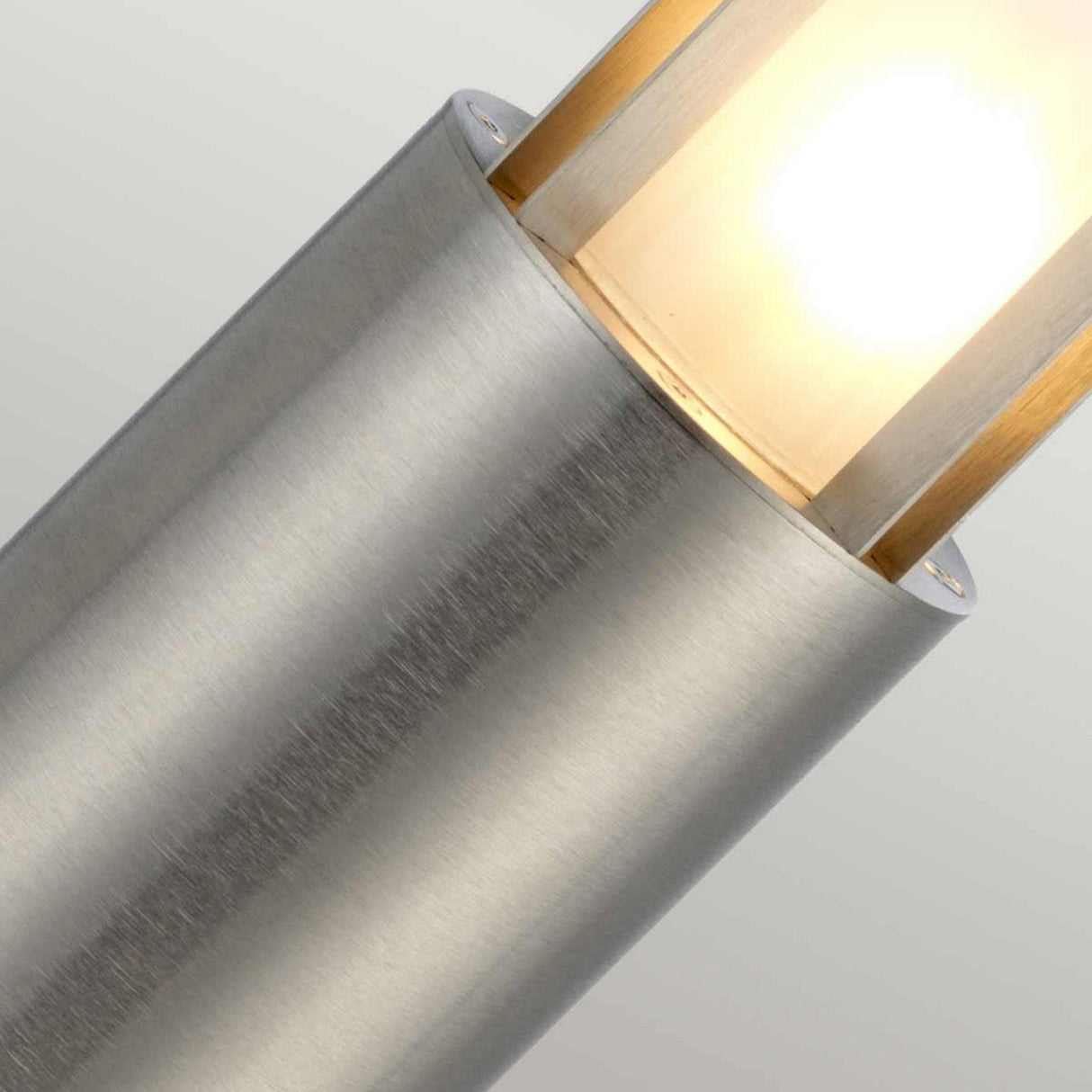 Close-up image of the Paignton 1 Light Mini Bollard in stainless steel, featuring a glowing bulb that highlights its sleek outdoor lighting design. The brushed stainless steel finish offers a stunning contrast to the soft, warm illumination against a neutral gray background.