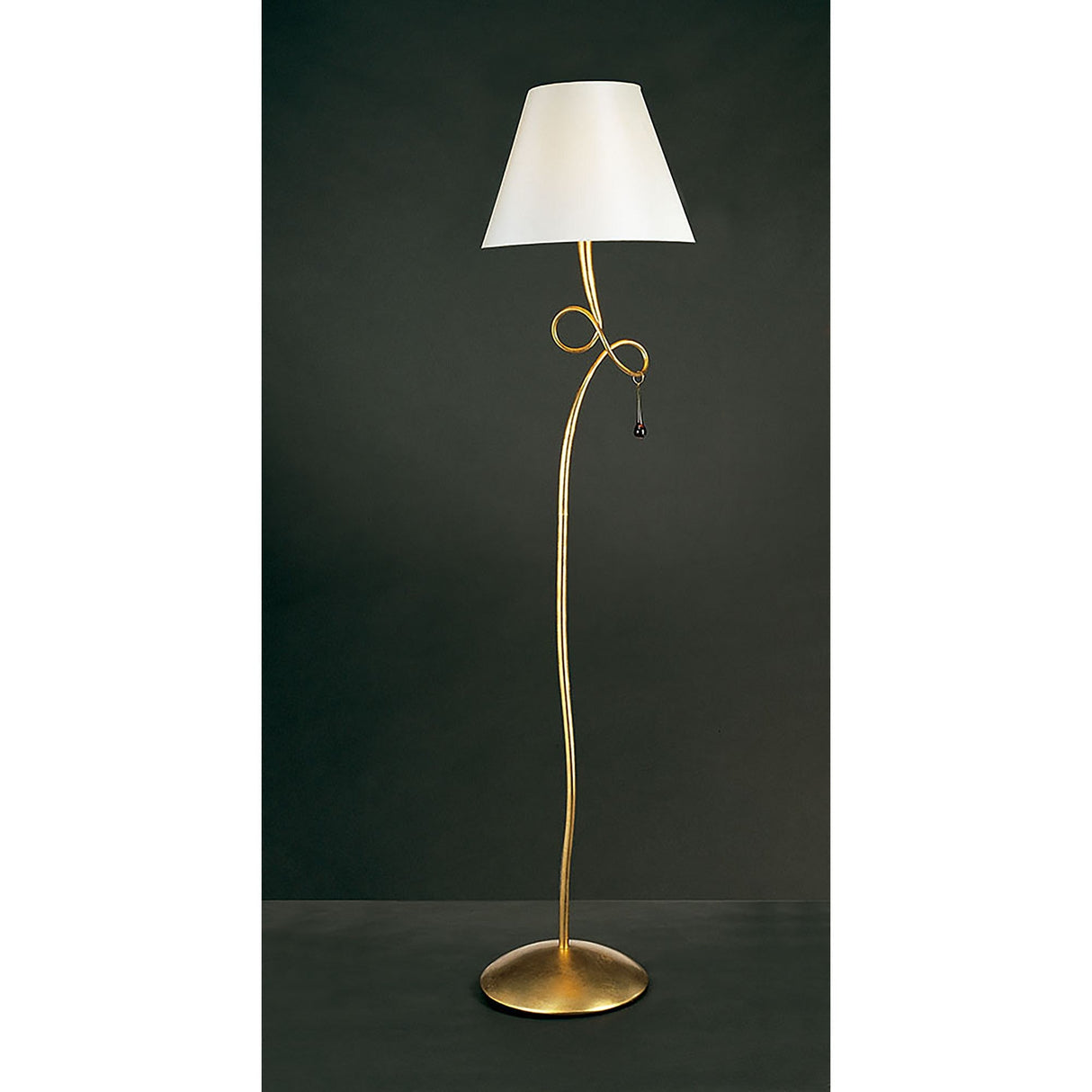 The Paola 1 Light Floor Lamp features a modern gold curved stand, circular base, decorative loop with glass droplets below a cream shade, all set against a dark background.
