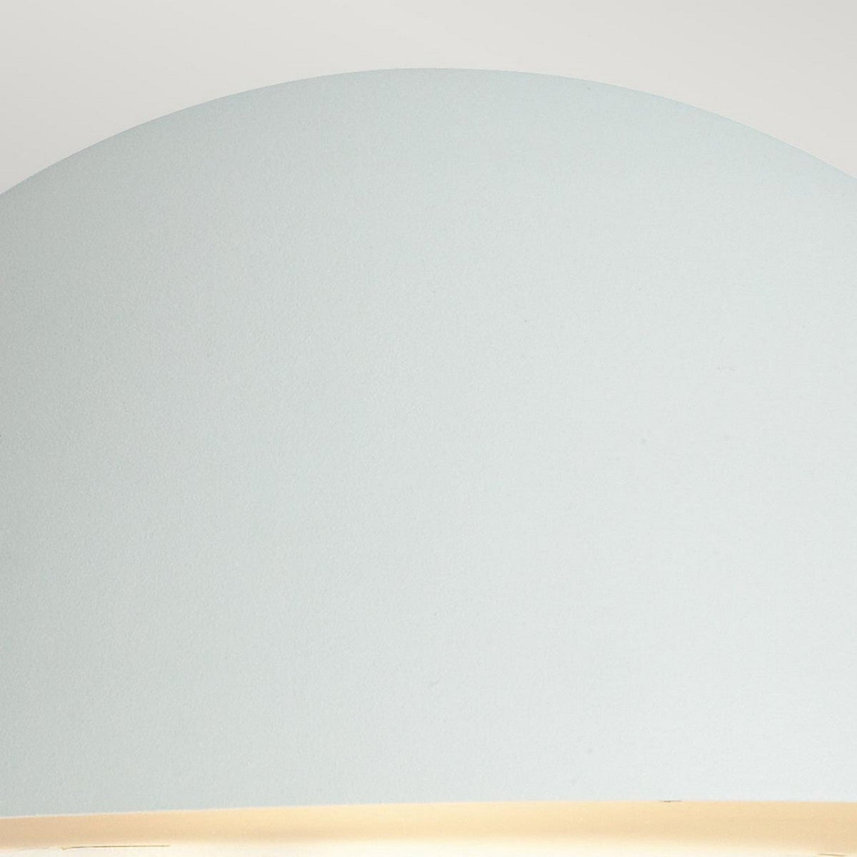 A close-up of a smooth, dome-shaped lampshade in pale blue, resembling a modern outdoor lighting piece, set against a light gray background. The bottom edge of this stylish Paris Outdoor Large 1 Light Wall Lantern - White emits a soft, warm glow.