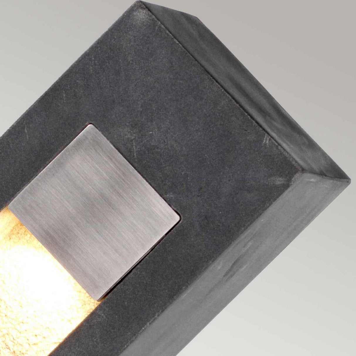 Introducing the Parkstone Large LED Bollard - a contemporary wall light featuring a rectangular design with a basalt stone finish, complemented by a brushed plate crafted from high-quality 316 stainless steel. This fixture casts a gentle glow downward against its solid light gray backdrop.