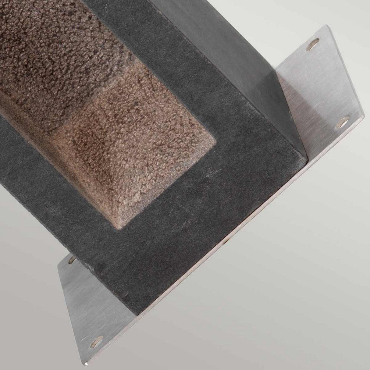 A close-up of the Parkstone Large LED Bollard showcases the textured surface of basalt stone alongside the smooth, polished edges of its 316 stainless steel components. The bollard forms a right angle, featuring visible mounting holes on its metal flanges.