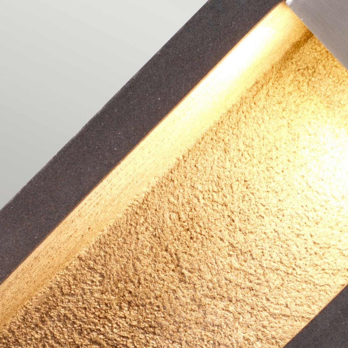 Close-up of the Parkstone Medium LED Bollard, featuring a sleek dark frame and a textured stainless steel interior reminiscent of basalt stone. The light casts a warm glow across the textured surface, accentuating its metallic sheen.