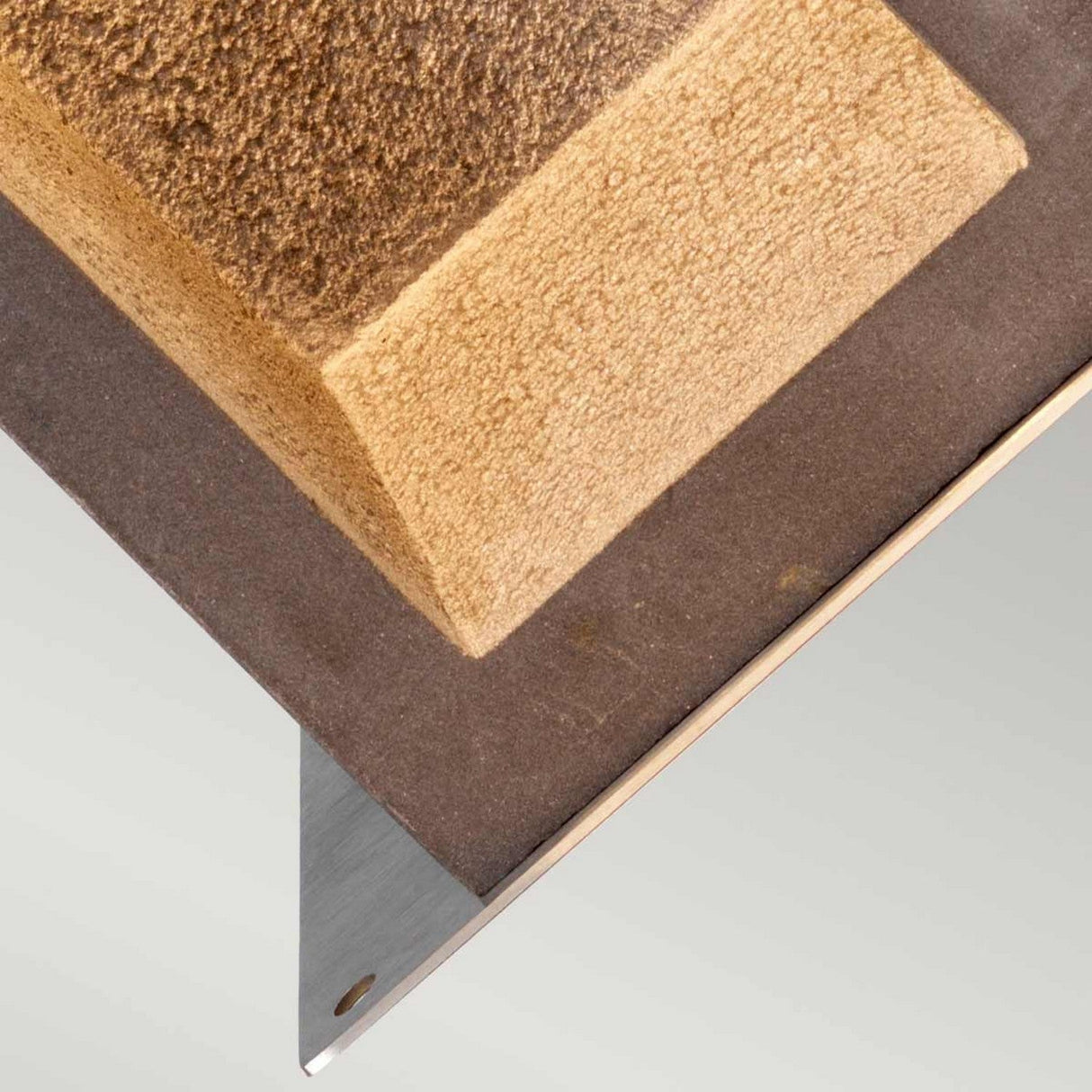 A close-up view showcases the Parkstone Medium LED Bollard, featuring a textured, triangular design resembling basalt stone. It is elegantly mounted on a sleek, angled stainless steel base against a plain background. The combination of textures and angles forms an abstract geometric composition that evokes modern outdoor lighting aesthetics.