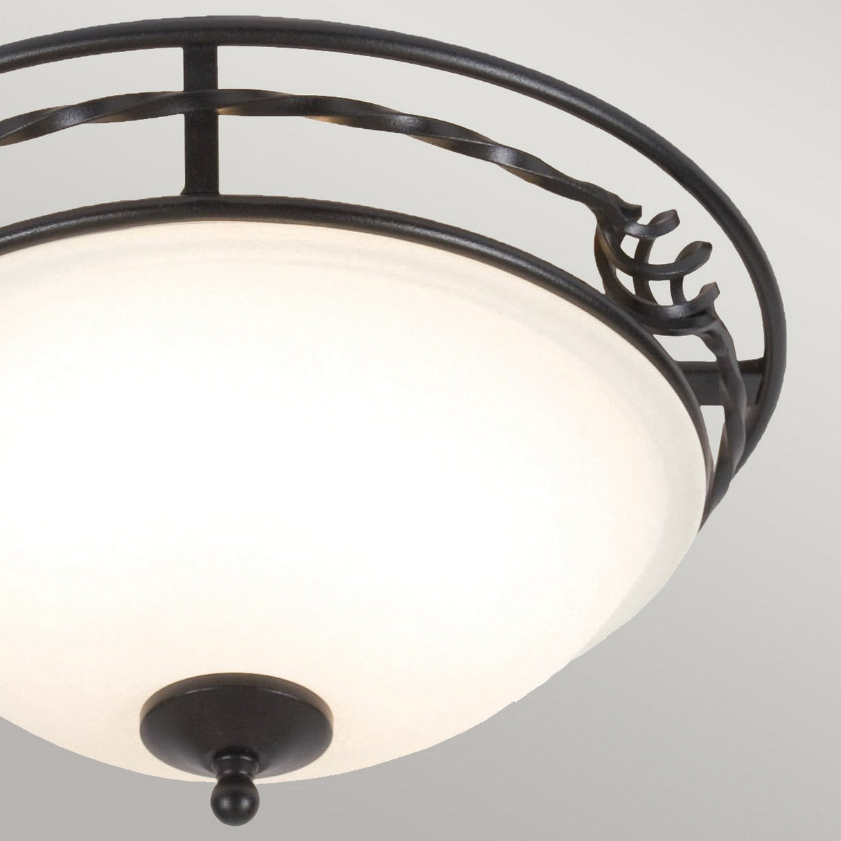 A detailed view of the Pembroke 2 Light Flush Light - Black highlights its frosted glass dome and intricate black metal frame. The hand-forged iron is adorned with decorative curves, and a small finial can be seen beneath the dome, showcasing elegance in this flush light design.