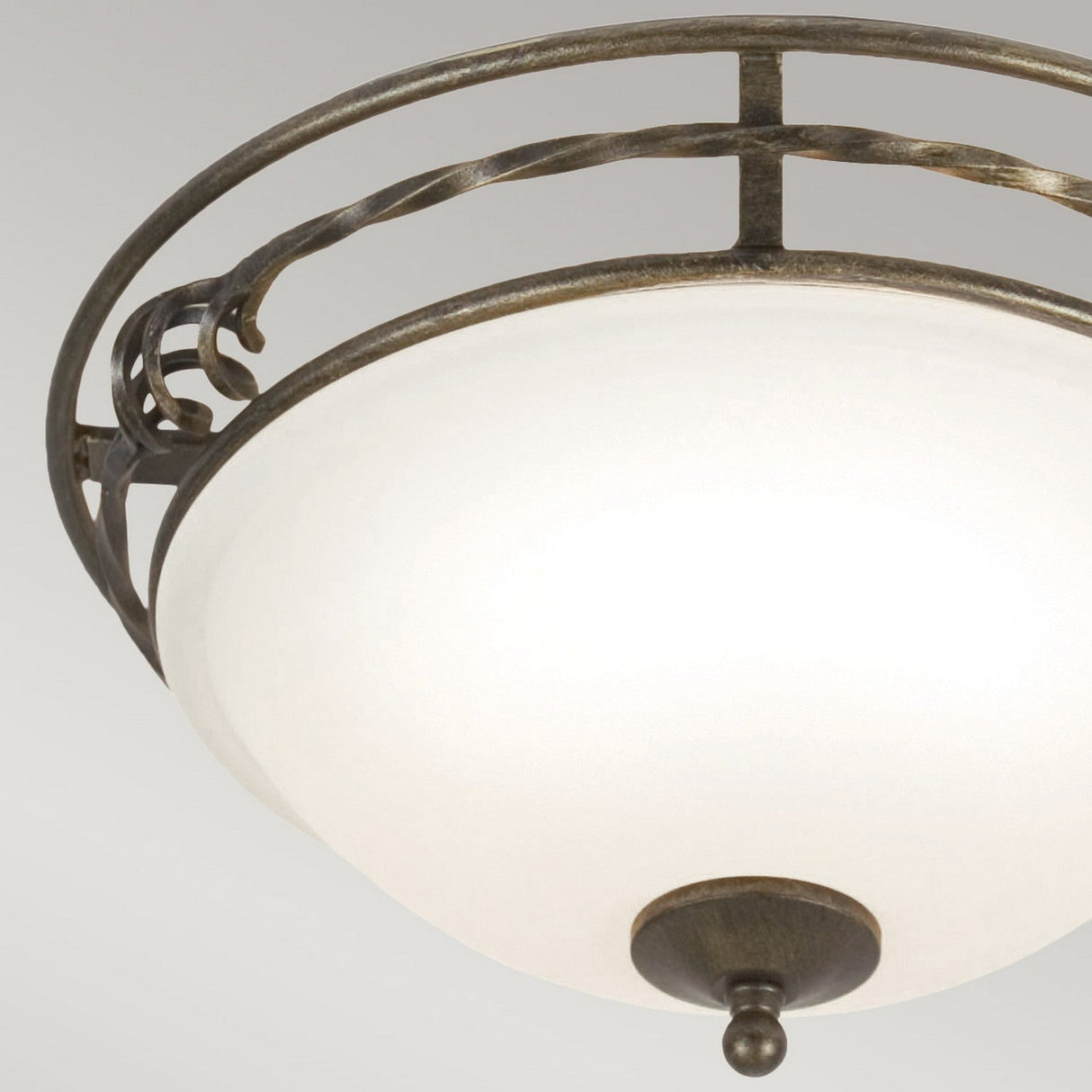A close-up of the Pembroke 2 Light Flush Light - Black/Gold reveals an elegant ceiling fixture with a frosted glass dome and gold metal accents against a pale gray background. Its decorative metal rim, crafted in hand-forged iron, features a swirled design, adding sophistication to the piece.