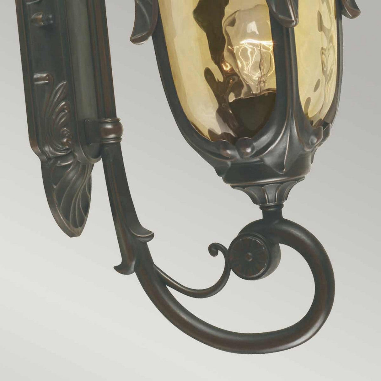 Close-up of the Philadelphia 1 Light Outdoor Medium Wall Light, featuring an ornate, antique-style design with a dark old bronze finish and an amber-colored glass cover. The intricate metalwork and decorative scrolls exude traditional elegance.