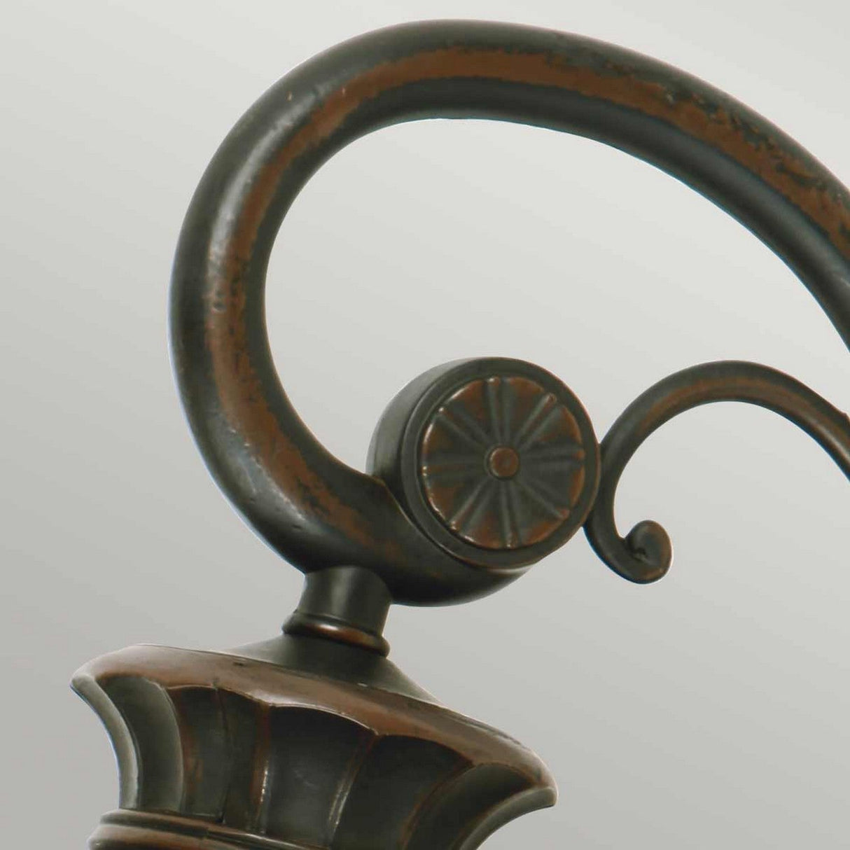 Close-up of the Philadelphia 3 Light Outdoor Large Down Wall Light in Old Bronze, showcasing an ornate handle with a dark, aged finish. The design features a curved loop and decorative circular elements with a flower-like pattern, exuding period charm. Attached to a base with ribbed details, it is reminiscent of the outdoor wall light fixture it adorns.