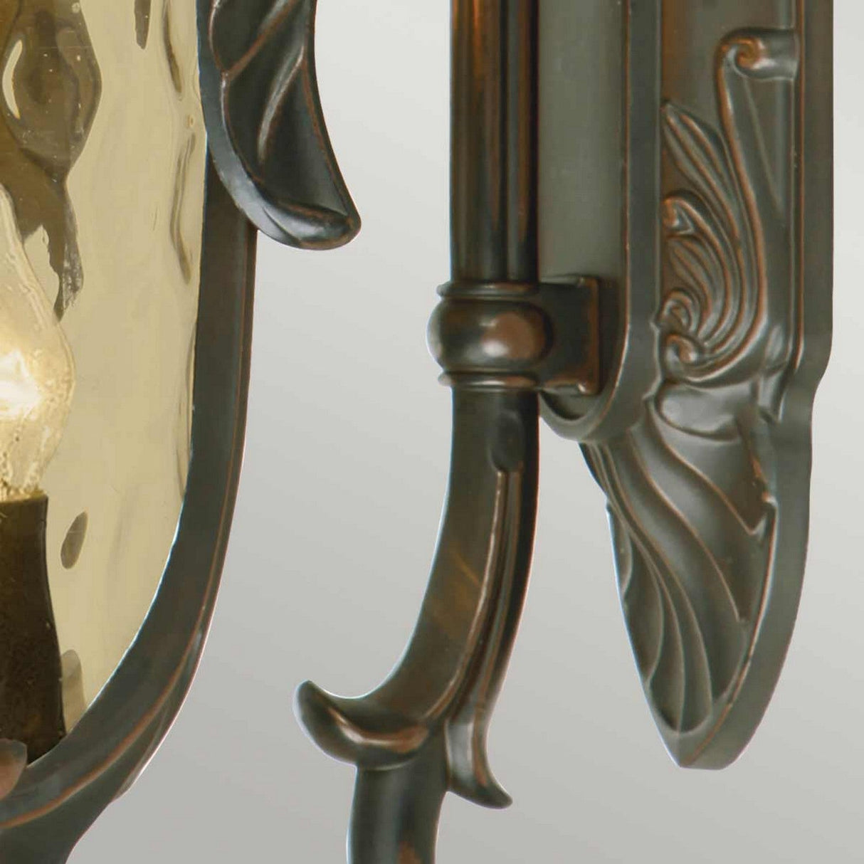 A detailed view of the Philadelphia 3 Light Outdoor Large Down Wall Light in an old bronze finish. The design radiates period charm with intricate carvings and a partially visible bulb encased in a textured glass cover.