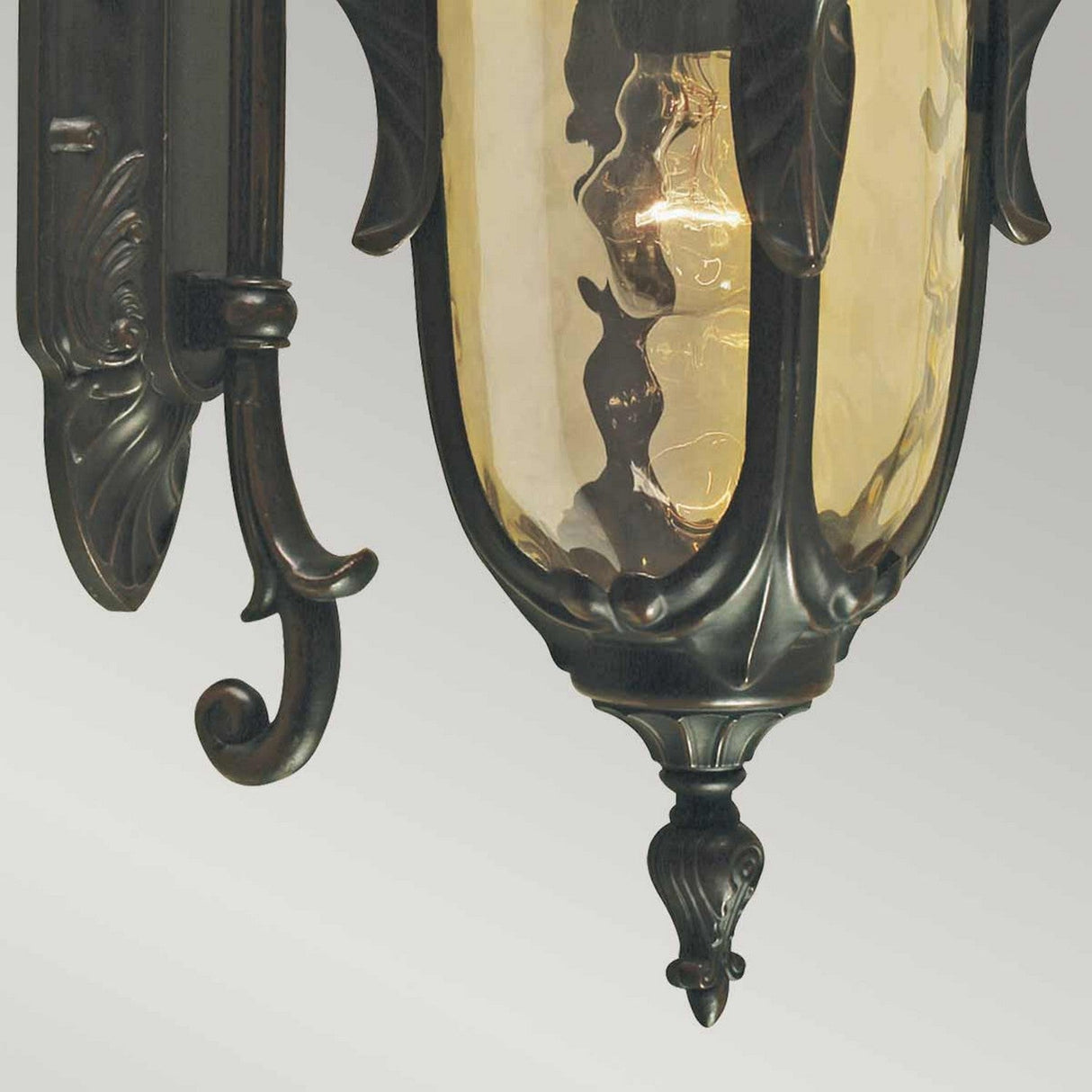 A detailed view of the Philadelphia 1 Light Outdoor Medium Down Wall Light - Old Bronze showcases its elegant, vintage-inspired design with a glowing bulb inside. This fixture is ideal for exterior use, boasting intricate metal craftsmanship in an Old Bronze finish and a glass shade with a warm amber tint that offers an inviting ambiance to outdoor spaces.
