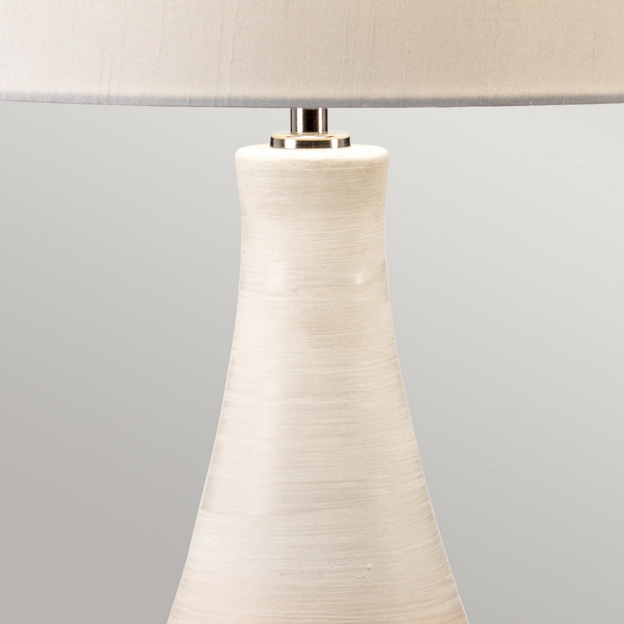 The Pinner 1 Light Table Lamp - Subtle Pink & Matt Cream showcases a subtle pink ceramic vase base with a smooth texture and a wide, slightly tapering design. It is beautifully complemented by a cream faux silk cylinder shade, set against a plain, light gray background.