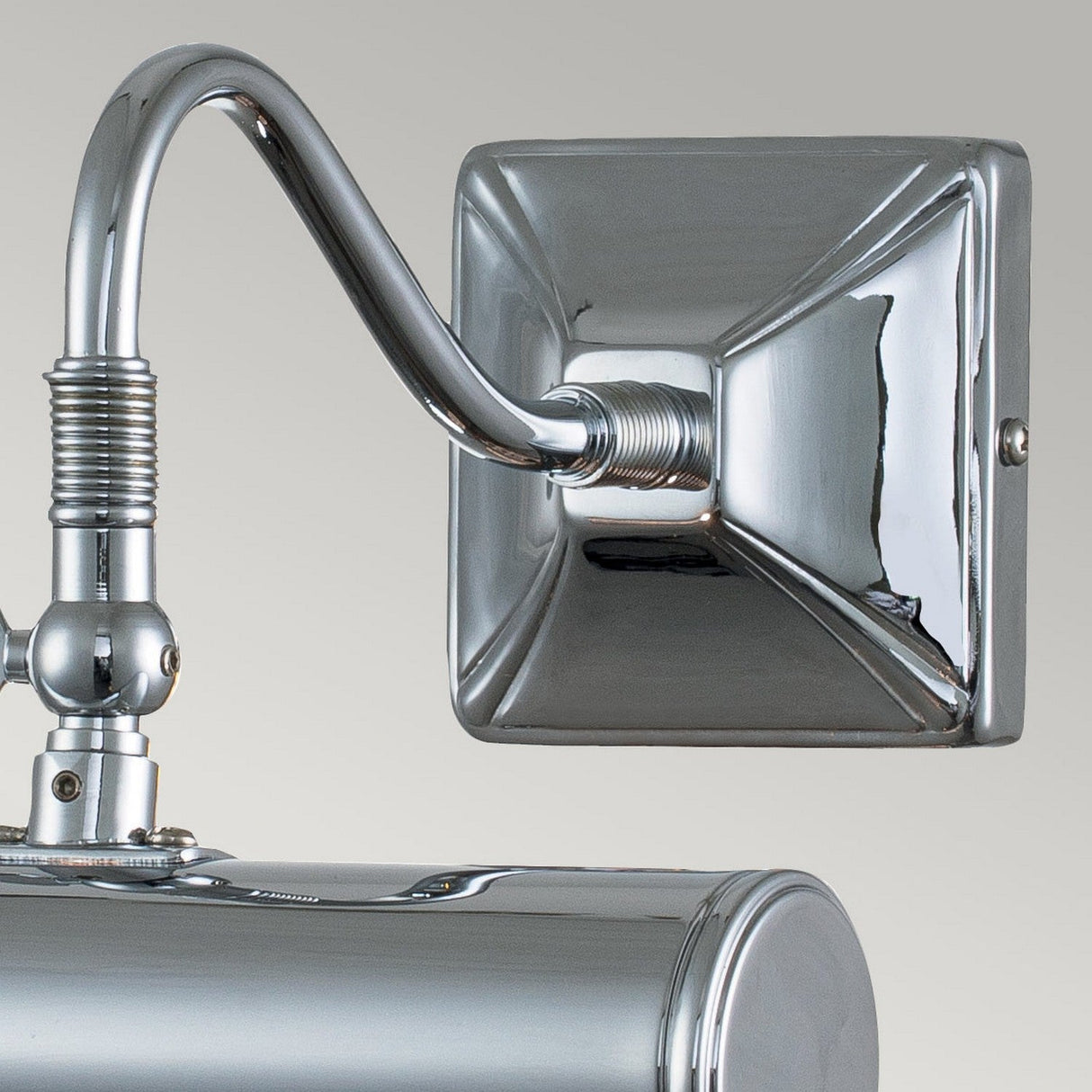 A close-up of the Picture Light 1 Light Small in Polished Chrome features a shiny finish. This wall-mounted light fixture highlights an angular backplate and a curved arm leading to a cylindrical shade. Its reflective, smooth surface stands out against a plain background, offering an elegant lighting solution.