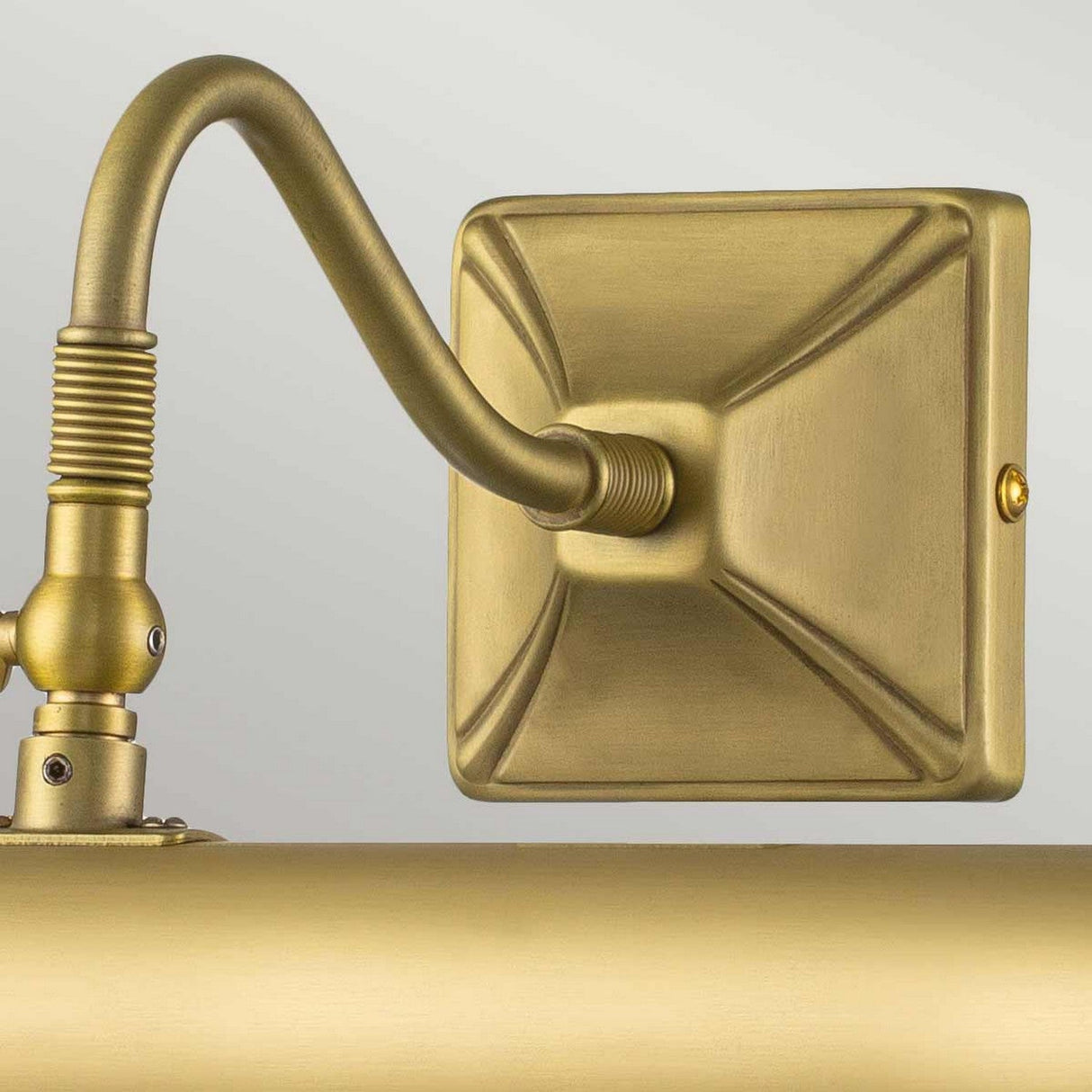 A close-up of the Picture Light 2 Light Large - Brushed Brass reveals its square backplate and elegantly curved arm. With a sleek design, it boasts a textured surface and adjustable lighting, making it perfect for showcasing art displays.