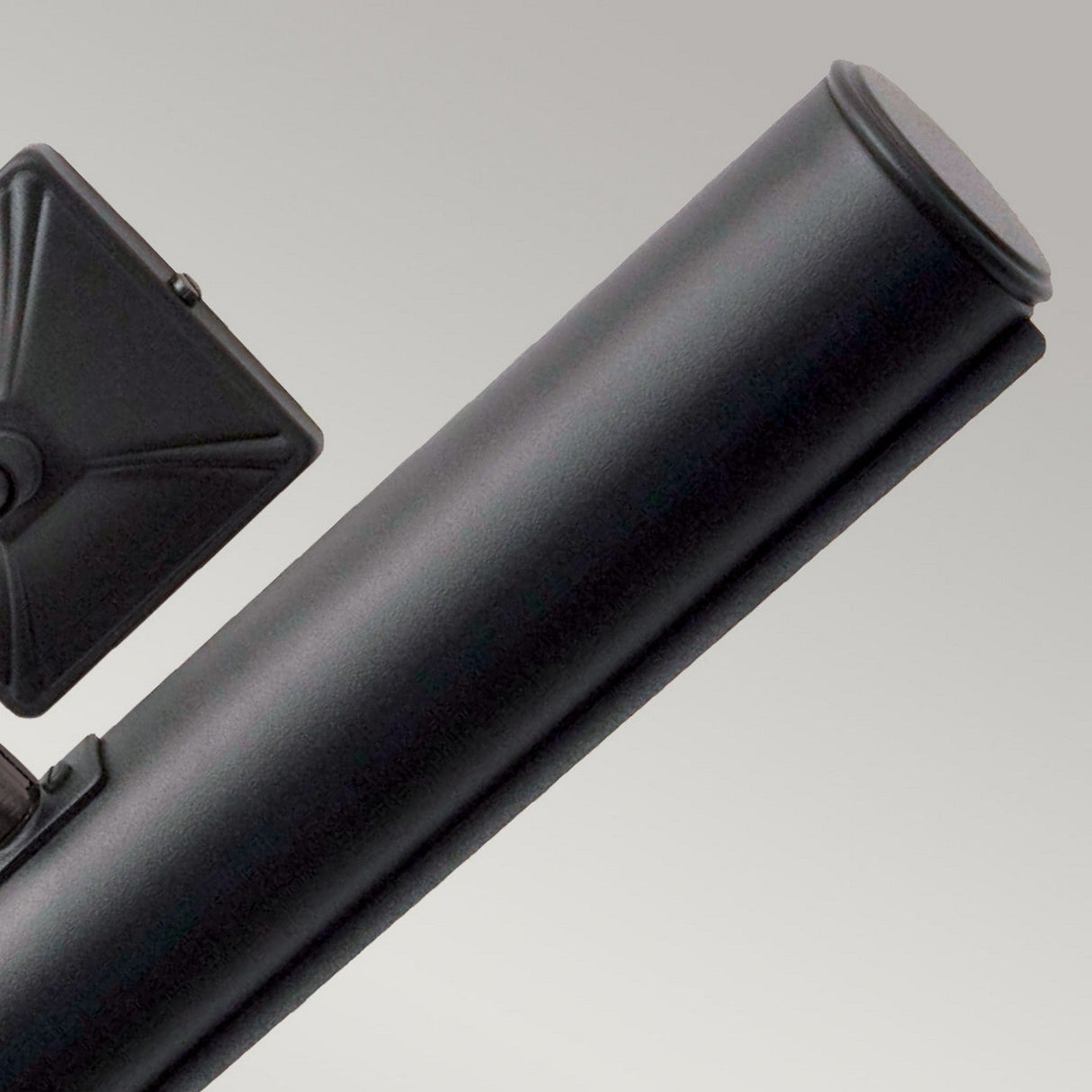 Close-up of a Picture Light 2 Light Large in black, its sleek form highlighted against a gray background with adjustable lighting. The softly angled light reveals its cylindrical body and diagonal design, almost as if poised to illuminate distant artwork.