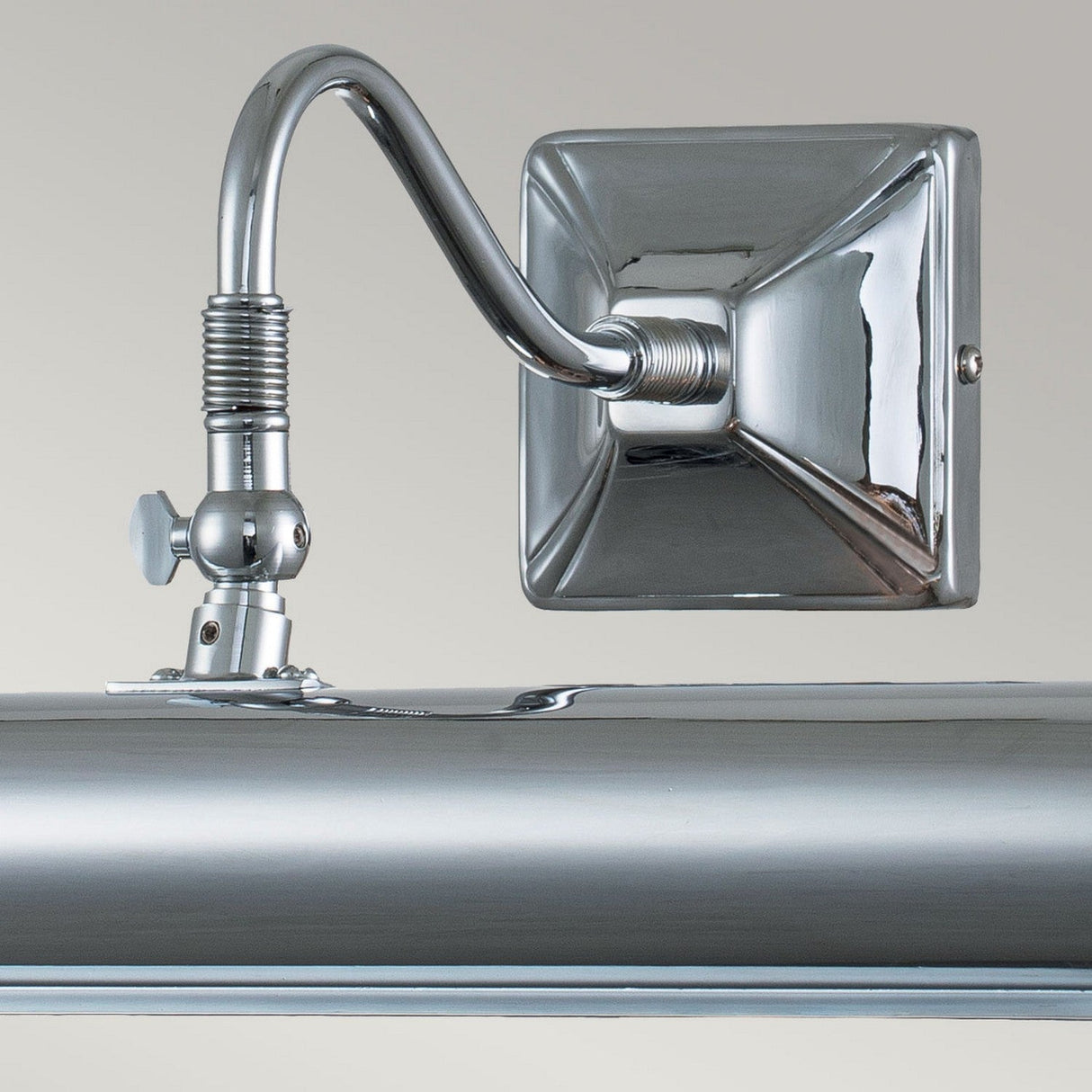 A close-up of the Picture Light 2 Light Large - Polished Chrome reveals its sleek, metallic wall-mounted design. It features a square base and a curved arm, with polished chrome beautifully reflecting light. The lamp includes adjustable lights controlled by a small knob on the side, making it perfect for any elegant setting.