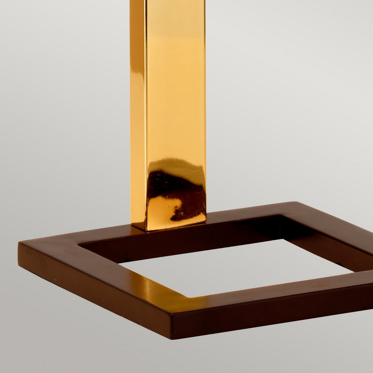 The Plein 1 Light Table Lamp in Dark Brown and Polished Gold showcases a polished gold vertical rod atop a dark brown square base, set against a plain light gray background that emphasizes its sleek modern design.