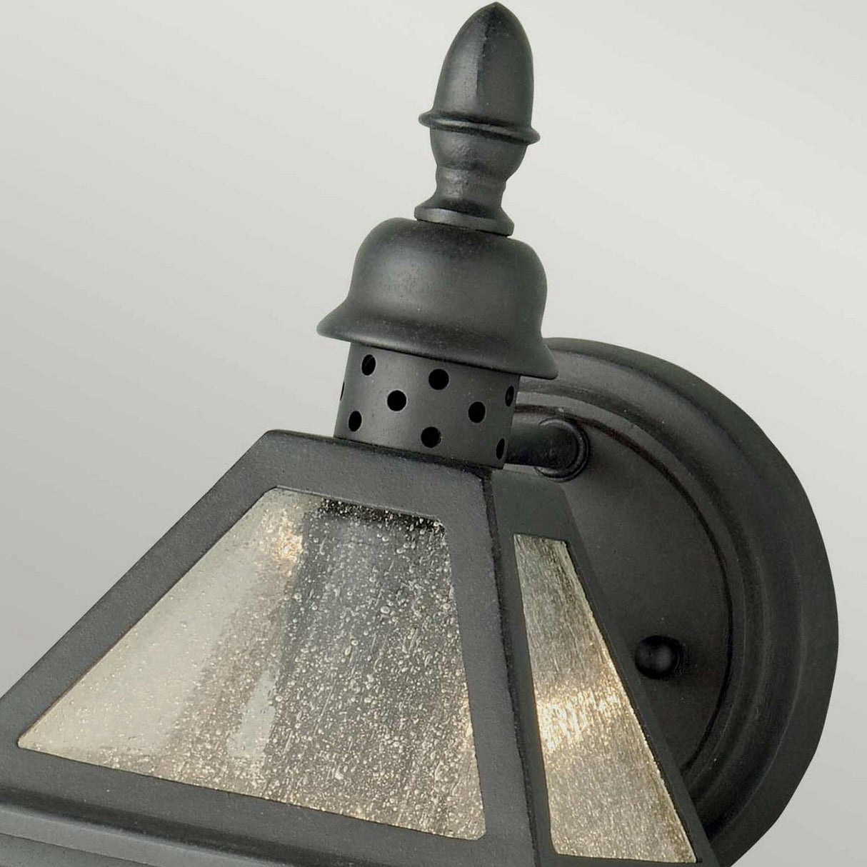 Close-up of the Polruan 1 Light Outdoor Wall Light in black, showcasing its classic design with IP44 rated protection, a pointed top, and seeded glass panels. The background is a neutral light gray.