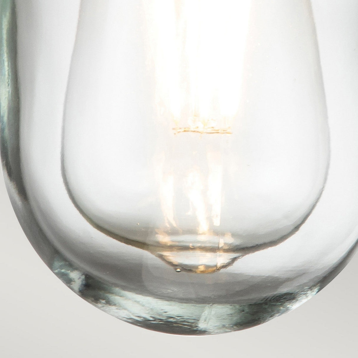 A close-up of a glowing light bulb with a visible filament is housed in the Porto 1 Light Outdoor Wall Light - Grey. The clear glass showcases the intricate details of the bulb's interior, and its nautical lantern design with a stainless-steel frame softly illuminates the surrounding surface.