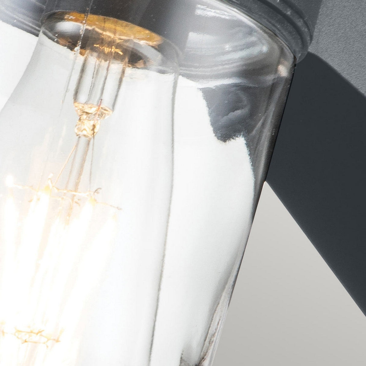 The Portfino 1 Light Outdoor Wall Light in grey features a clear glass bulb emitting warm light reminiscent of nautical lighting. Its intricate filament is visible against a gray background, and the metallic screw base adds a classic design touch.