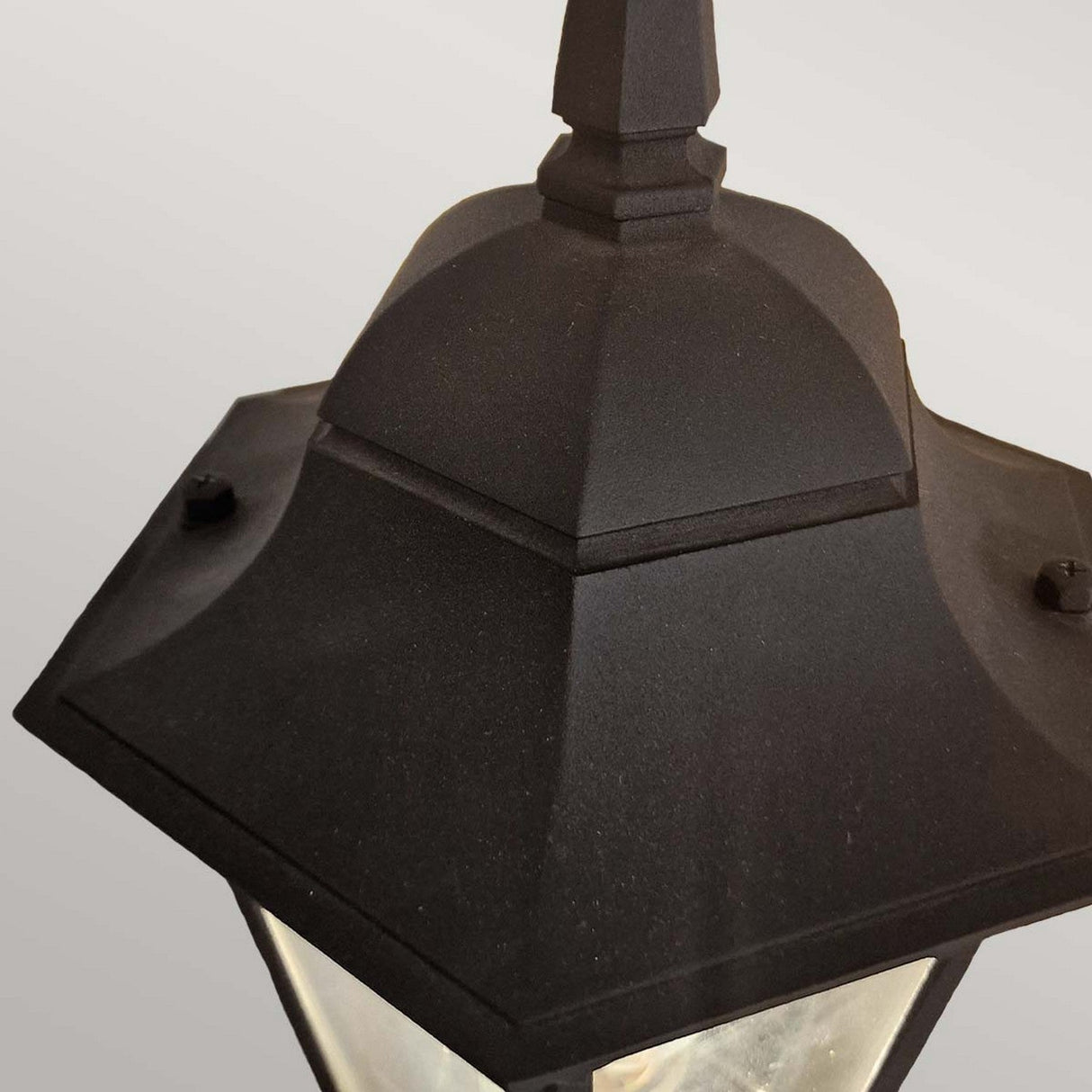 Here is a description using the provided product data:
Close-up of the Parish 1 Light Outdoor Down Wall Light in a black powder-coated finish, showcasing its hexagonal design. This lantern, made from die-cast aluminum, includes glass panels and a small decorative finial on top, displayed against a plain gray background.