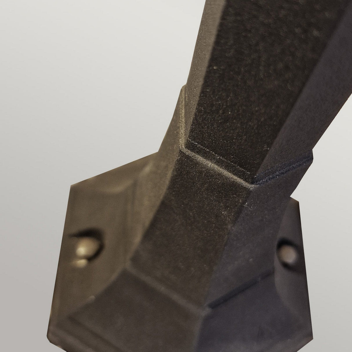 Close-up of the Parish 1 Light Pillar Light in black, featuring an angular metal design with a textured surface. It is mounted on a base with two visible screws against a white background, resembling elements commonly used in garden pathways.