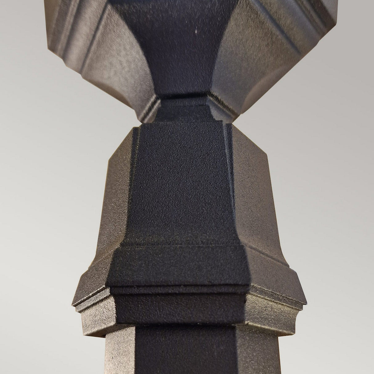 Close-up of the Parish 1 Light Lamp Post - Black, a geometric sculpted object made from die-cast aluminum with a textured surface. The plain light gray background highlights the intricate design of this outdoor lighting fixture.