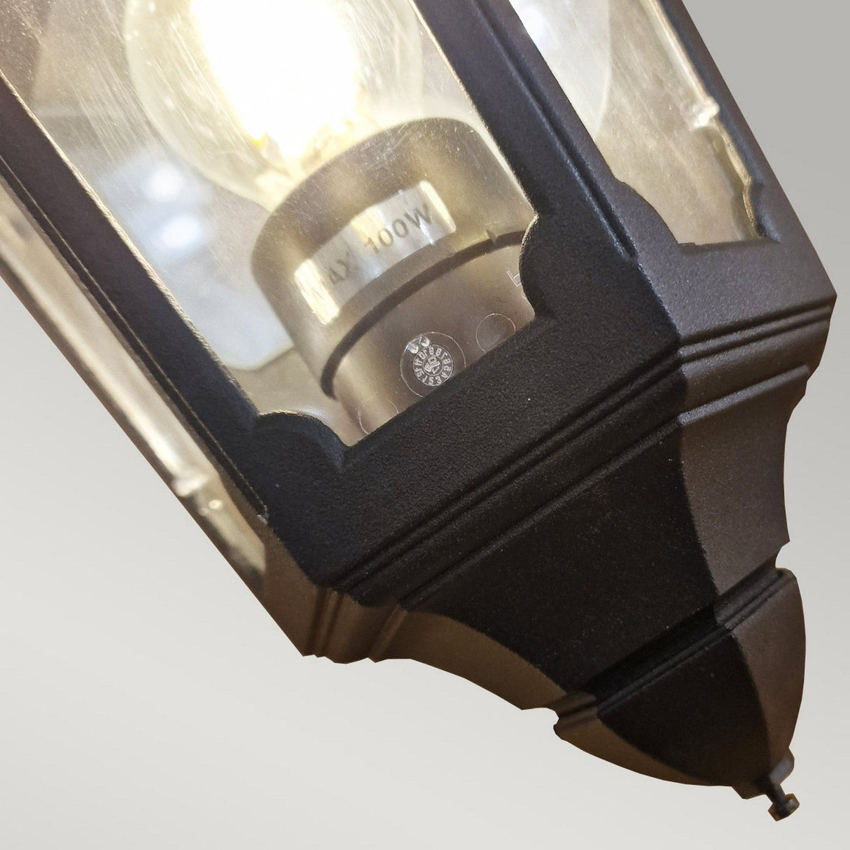 Close-up of the Parish 1 Light Outdoor Wall Light in black, featuring a glass enclosure that reveals the visible light bulb inside. Made from durable die-cast aluminum, its intricate metal frame emphasizes its IP44 rating, ensuring it provides a warm glow regardless of the weather conditions.