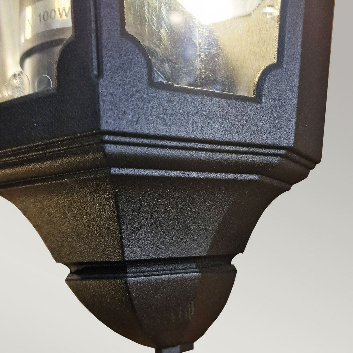 A close-up view of the Parish 1 Light Outdoor Wall Light in black, showcasing its textured die-cast aluminum finish. The lantern includes clear glass panels and a visible bulb that emits a warm glow. With its IP44 rating, this fixture is ideal for various weather conditions. The background features a soft gray hue.