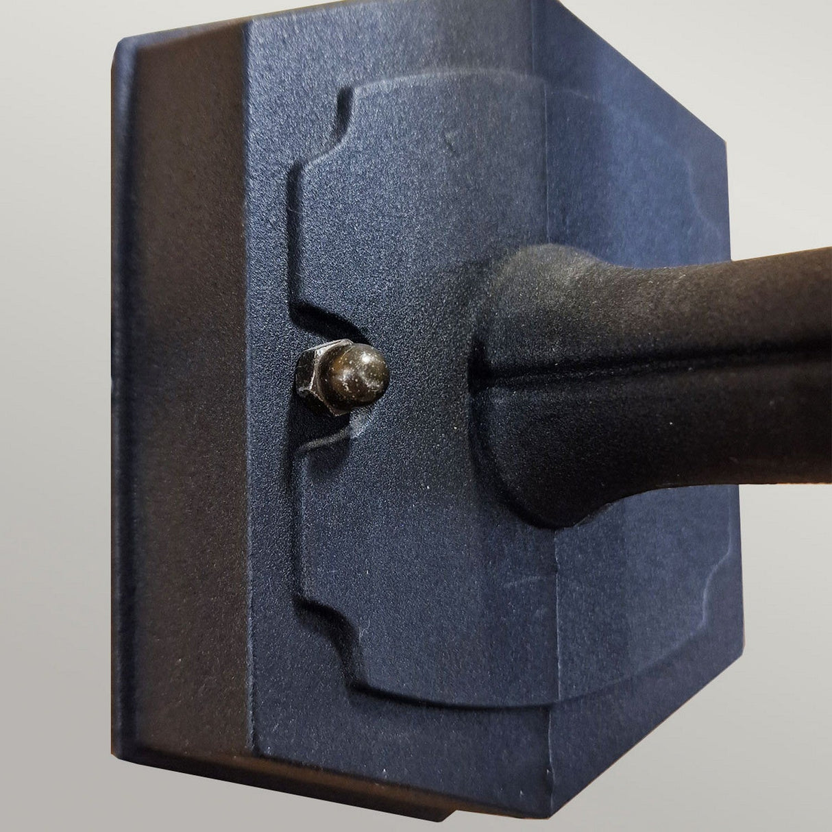 Close-up view of the Parish Mini 1 Light Outdoor Up Wall Light in black, showcasing its dark-colored die-cast aluminum construction. It features a rectangular panel with a protruding bolt on the side, set against a neutral light gray background.