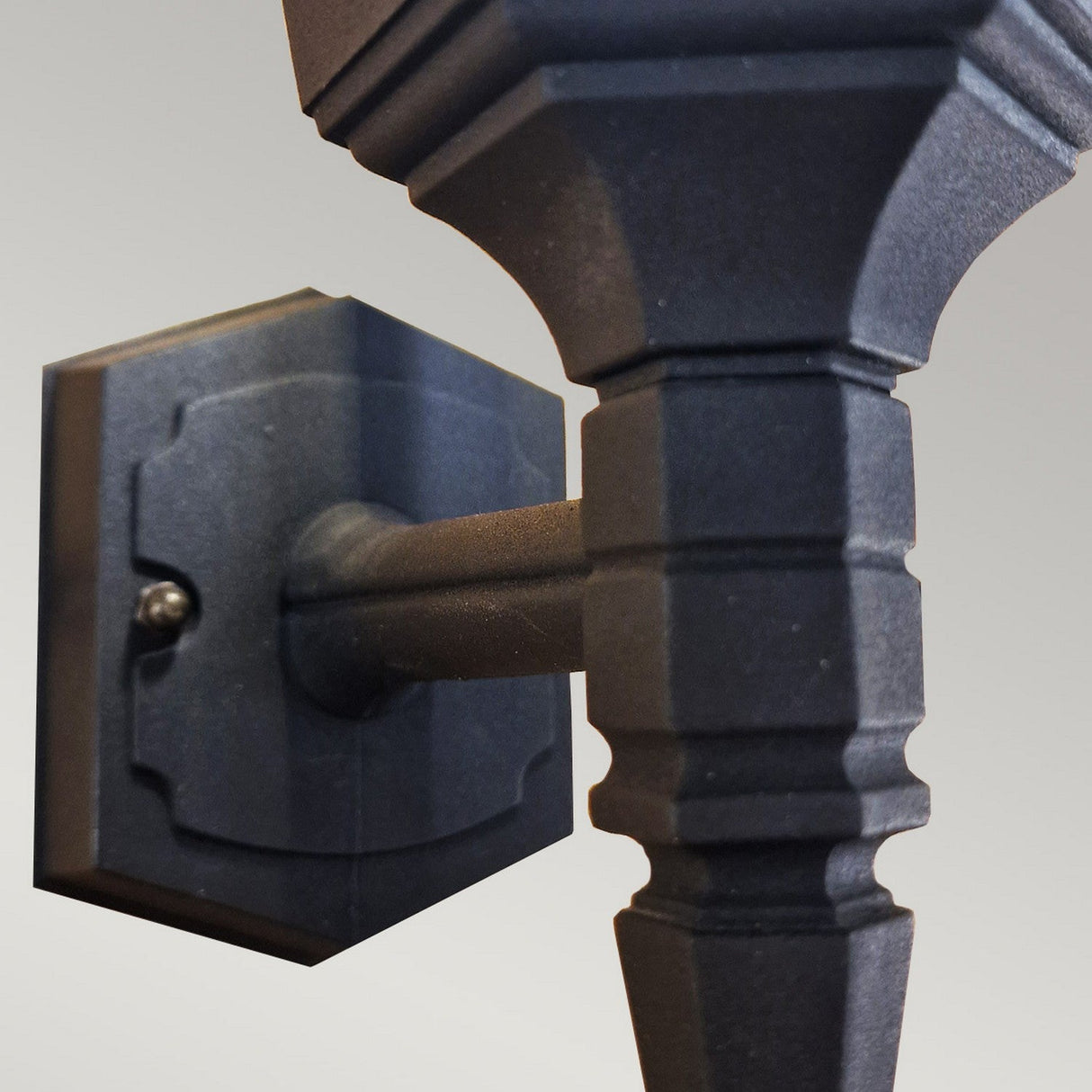 Capture the elegance of the Parish Mini 1 Light Outdoor Up Wall Light in black, featuring a geometric design meticulously crafted from die-cast aluminum. This outdoor fixture showcases a hexagonal base and an intricately detailed pole that expands into a broader section, all complemented by a muted gray backdrop. With an IP44 rating, it is ideal for outdoor settings.