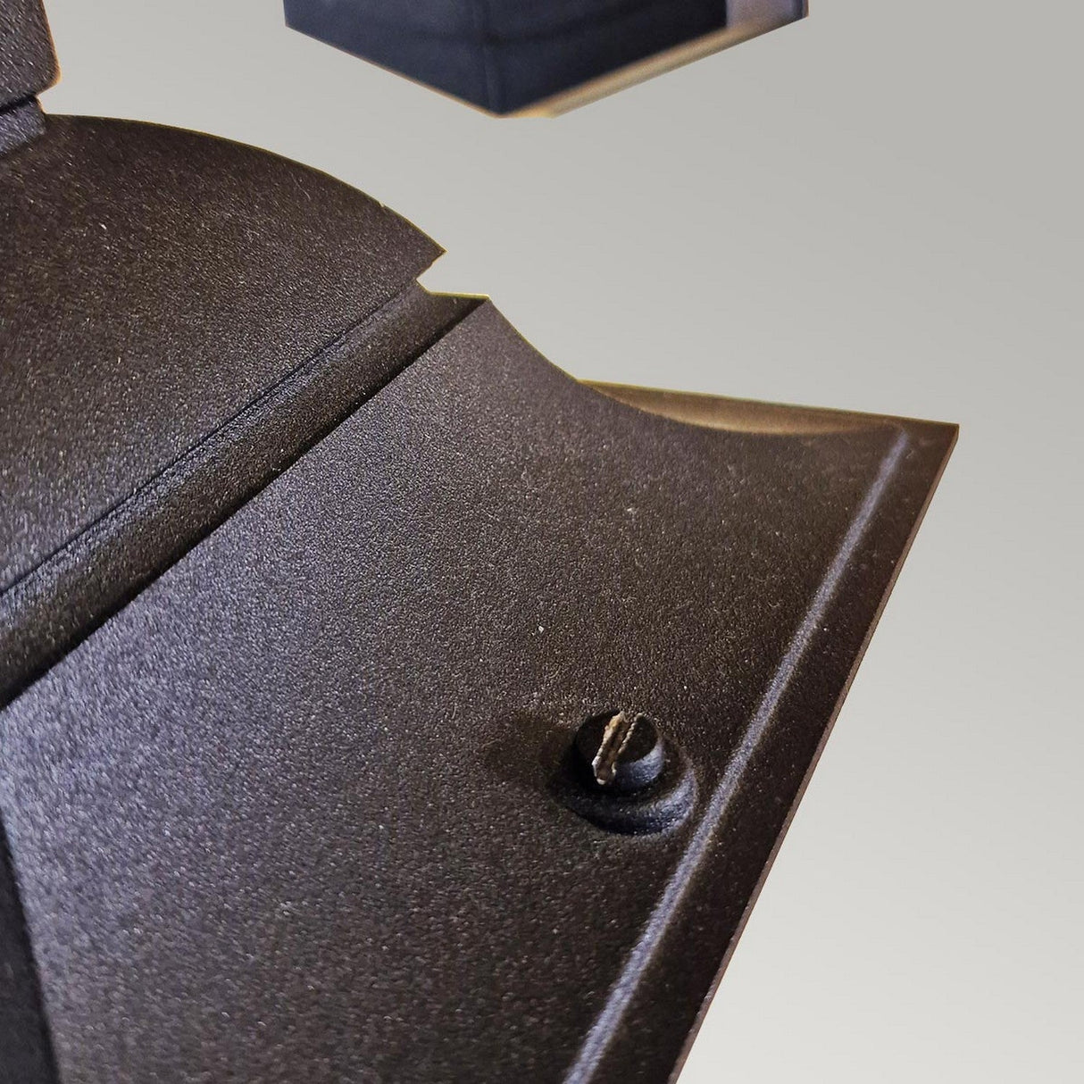 Close-up of the Parish Mini 1 Outdoor Light Down Wall Light in black metal, showcasing a screw on its textured surface. The light gray background is slightly blurred to emphasize the outdoor fixture.