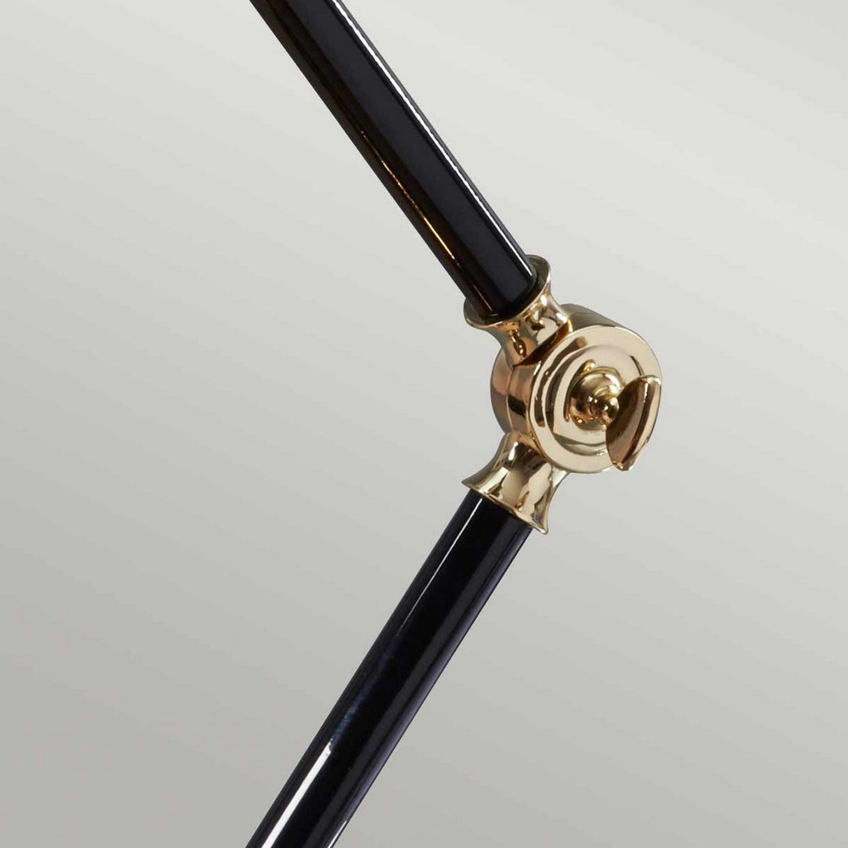 Close-up of two metallic rods connected by the polished brass joint of the Provence Element 1 Light Mini Table Lamp, set against a light gray background. The shiny joint contributes a French-inspired design to the composition, with one rod angled upward and the other extending downward, evoking an elegant Provence element.