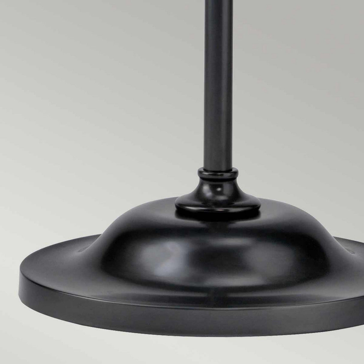 A close-up of the Provence 1 Light Floor Lamp showcases its black metal base with a smooth, round design and a narrow vertical pole extending upward. The vintage-inspired appearance is highlighted by an Old Bronze finish, set against a neutral gray background.