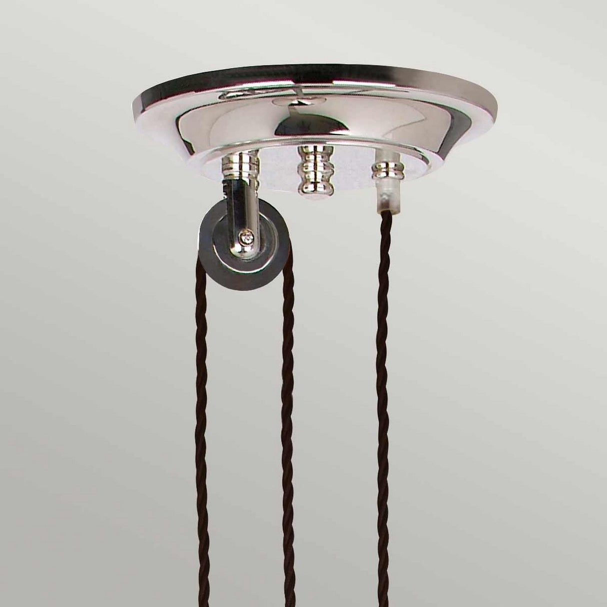 A close-up of the Provence 1 Light Rise & Fall Pendant in polished nickel showcases two twisted brown fabric cables elegantly hanging from it. The fixture features two attachment points and a small, round, dark gray component to the side.