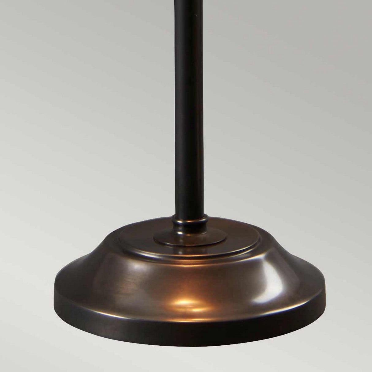 The close-up reveals the Provence 1 Light Stick Lamp in old bronze, showcasing a smooth, glossy finish. Its simple, rounded design complements the vertical pole extending upwards. The ambient downlighting effect is highlighted against a plain, light gray background.