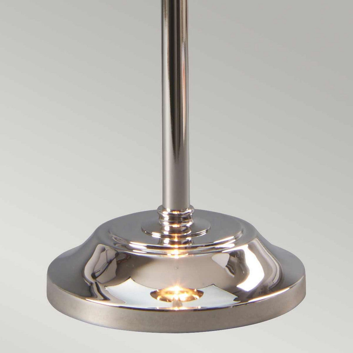 The Provence 1 Light Stick Lamp - Polished Nickel showcases a polished nickel circular base supporting a sleek metallic rod. Its shiny surface elegantly reflects light against a plain, light gray background, making it an ideal choice for ambient downlighting in any sophisticated setting.