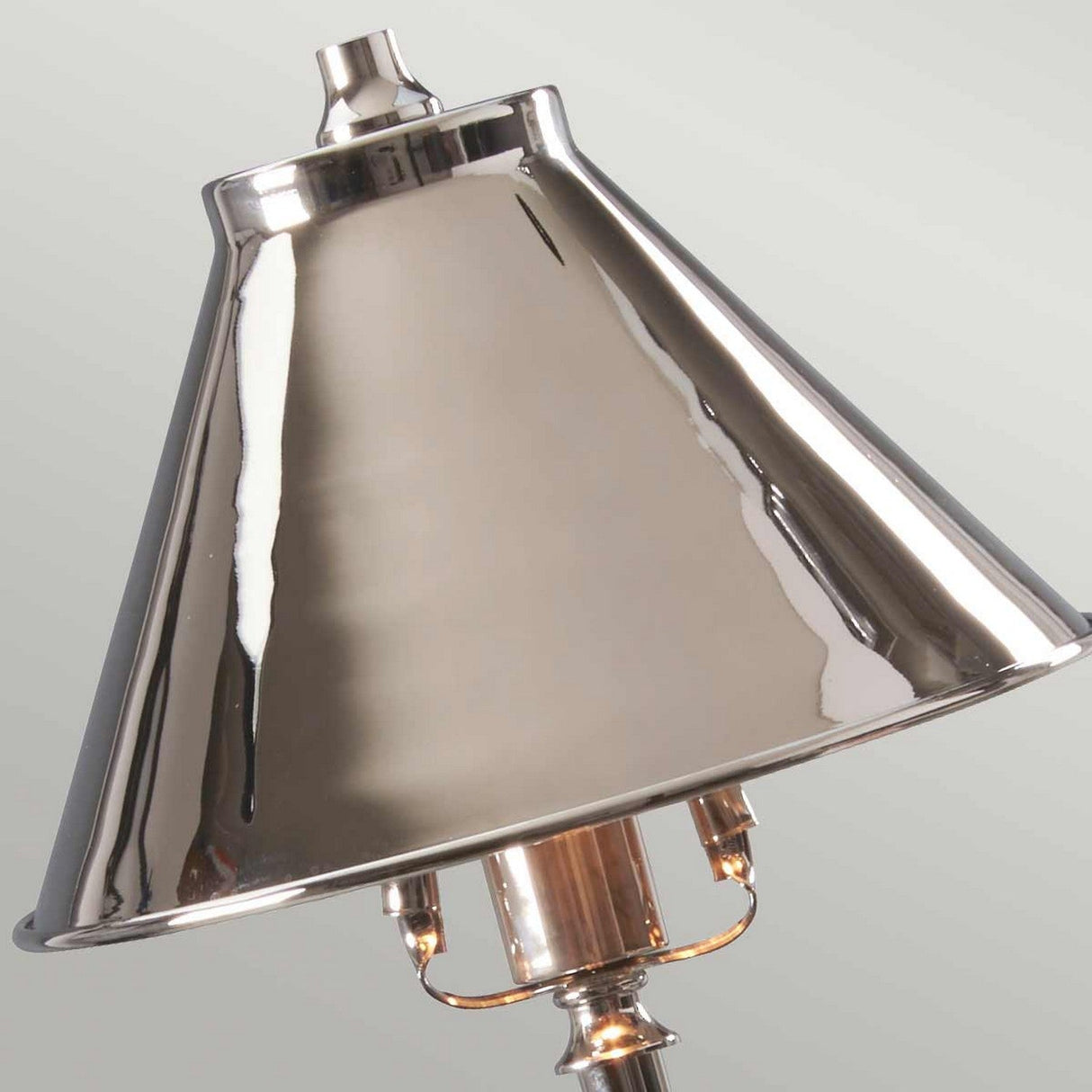 A close-up view of the Provence 1 Light Stick Lamp in polished nickel reveals its shiny, reflective surface. This lamp features a conical shape, providing ambient downlighting with the light bulb partially visible beneath it. The background showcases a plain, light-colored wall.