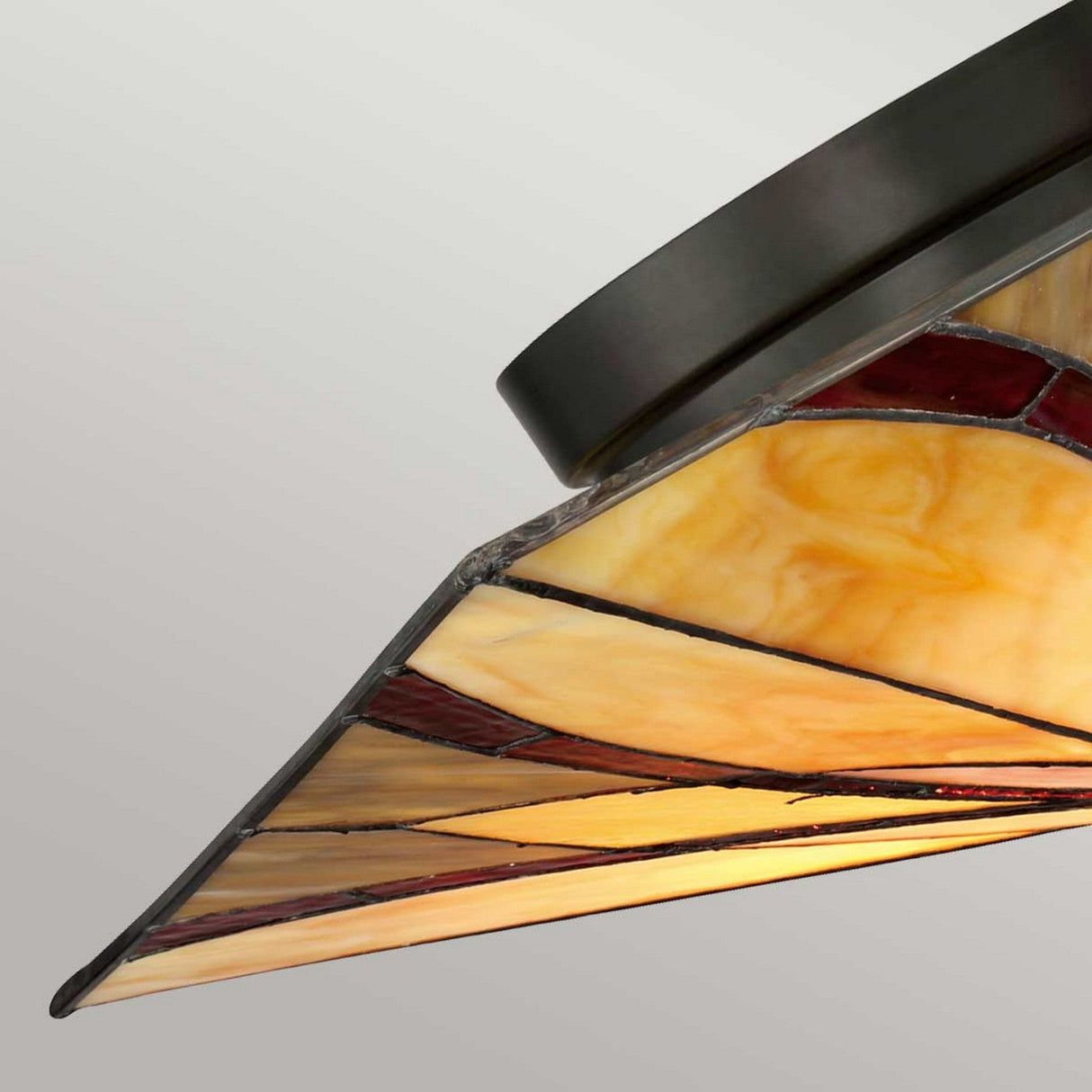 A close-up of the Asheville 2 Light Tiffany Flush - Valiant Bronze showcases a stained glass ceiling lamp featuring a geometric design with warm yellows and reds, framed by Valiant Bronze metal. The neutral backdrop enhances its intricate pattern and vibrant colors.