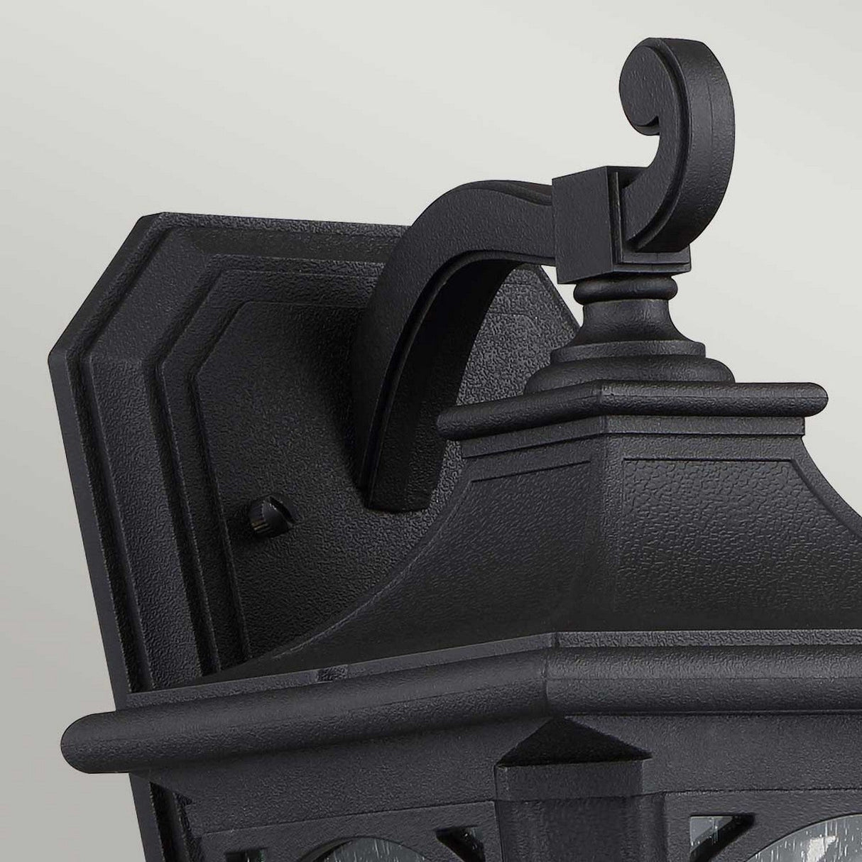 Presenting the Bedford Outdoor 1 Light Small Wall Lantern in black, this fixture is crafted from durable composite material with intricate metalwork. It showcases a curved arm and decorative top, elegantly mounted on a rectangular backplate, combining traditional and modern design elements seamlessly.