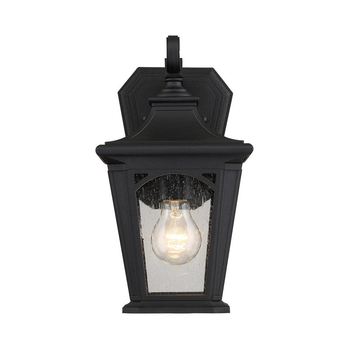 The Bedford Outdoor 1 Light Small Wall Lantern - Black boasts a classic design with vintage lighting appeal, featuring clear glass panels that reveal a visible incandescent bulb. Its frame has a slightly weathered texture and is crafted from durable composite material, all set against a plain white background.
