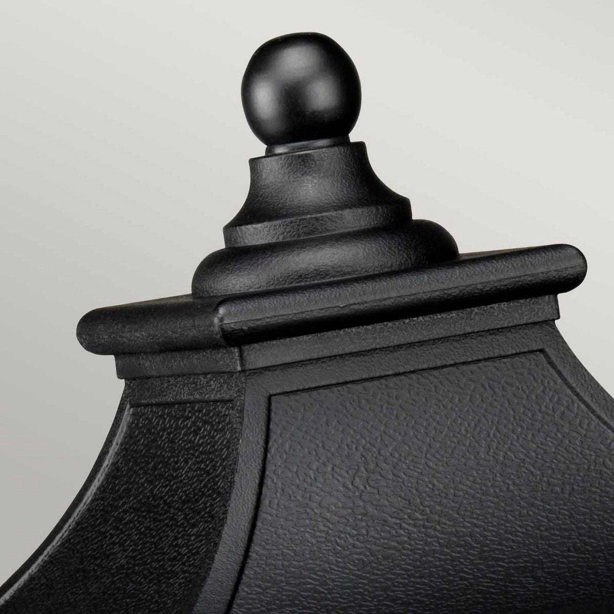 Close-up of a black, ornate finial on top of a decorative structure exuding vintage charm, showcasing a textured surface with a round knob at its peak. The background features a soft gradient of light gray, evocative of the style of the Bedford 1 Light Medium Pedestal Lantern - Black.