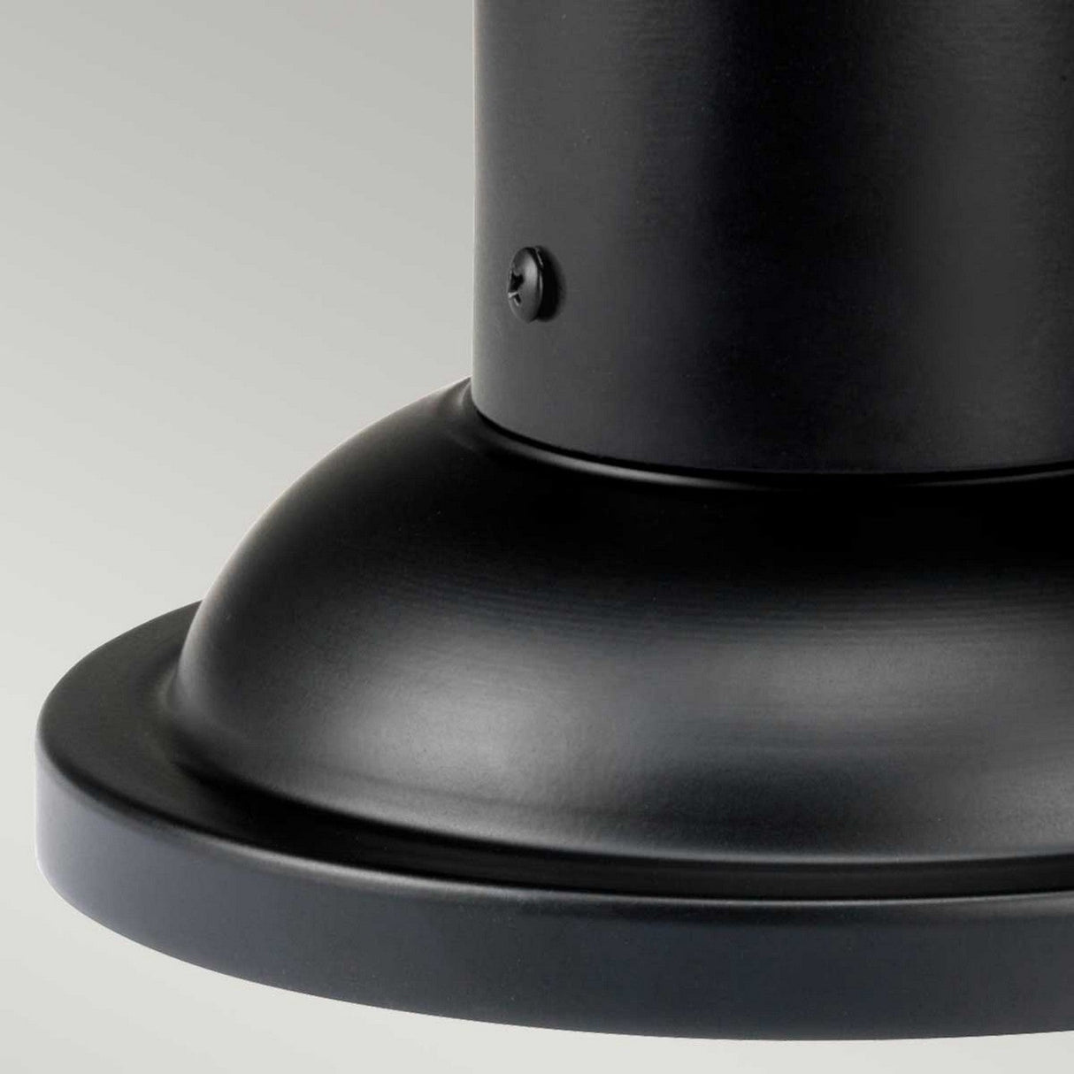 Close-up of the sleek black metal base of the Bedford 1 Light Medium Pedestal Lantern, featuring smooth curves and a matte finish, exuding vintage charm against a plain light gray background.