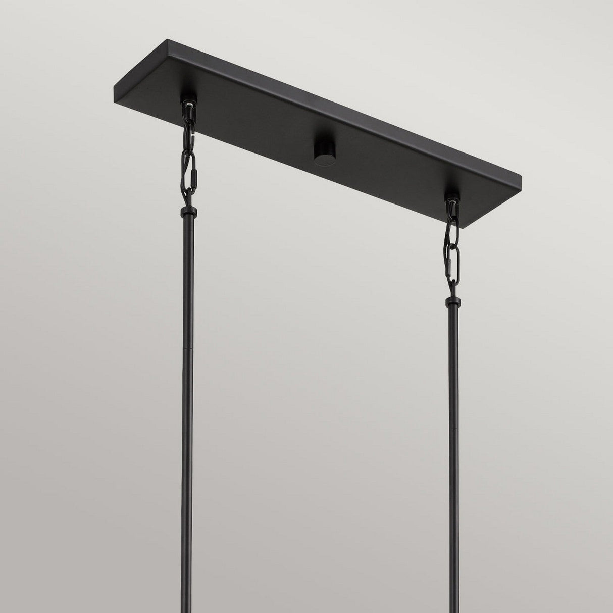 The Bismarck 5 Light Linear Pendant - Black radiates modern elegance with its sleek, minimalist design and rectangular base. Ideal for positioning above kitchen islands, it boasts two chic hanging rods set against a simple gray backdrop, adding a touch of distinctive style.