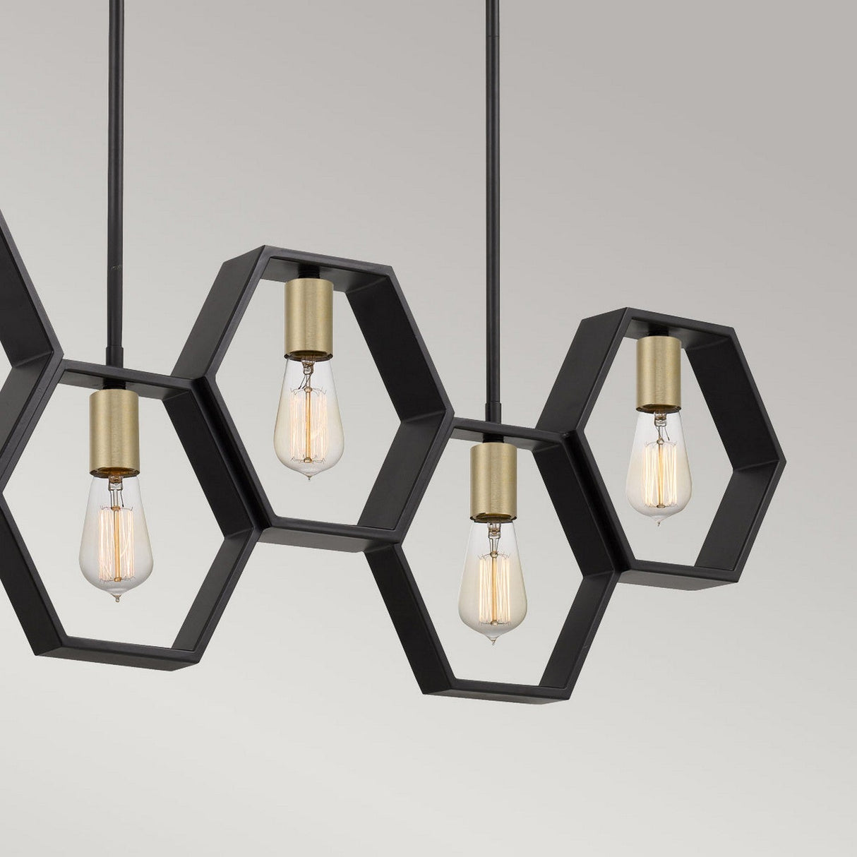 The Bismarck 5 Light Linear Pendant - Black radiates modern sophistication through its hexagonal black metal frames, elegantly housing exposed bulbs. Ideal for kitchen islands, this fixture showcases five bulbs hanging from the ceiling in a captivating geometric arrangement.
